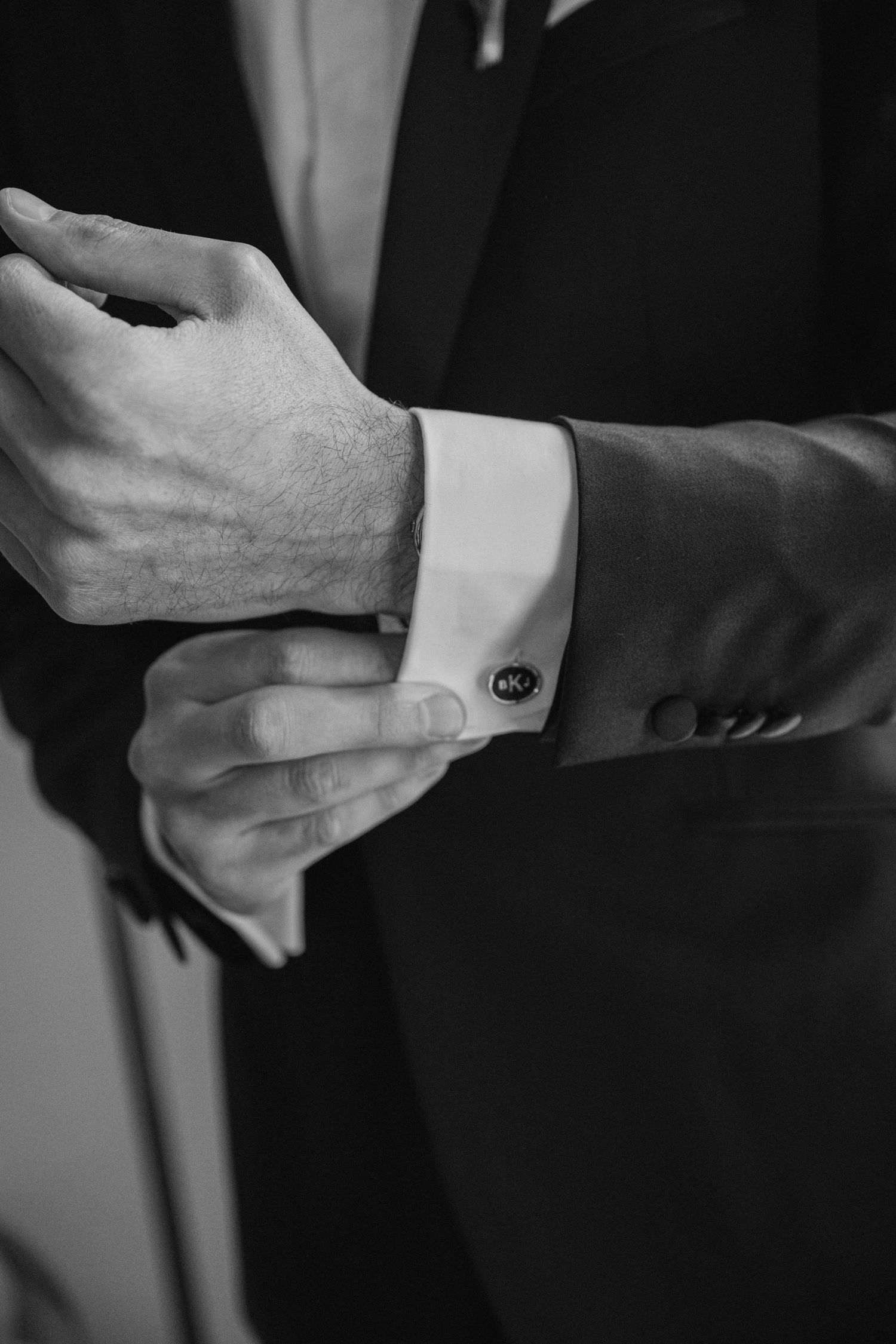 Close-up black and white shot of hands adjusting formal suit cufflinks.
