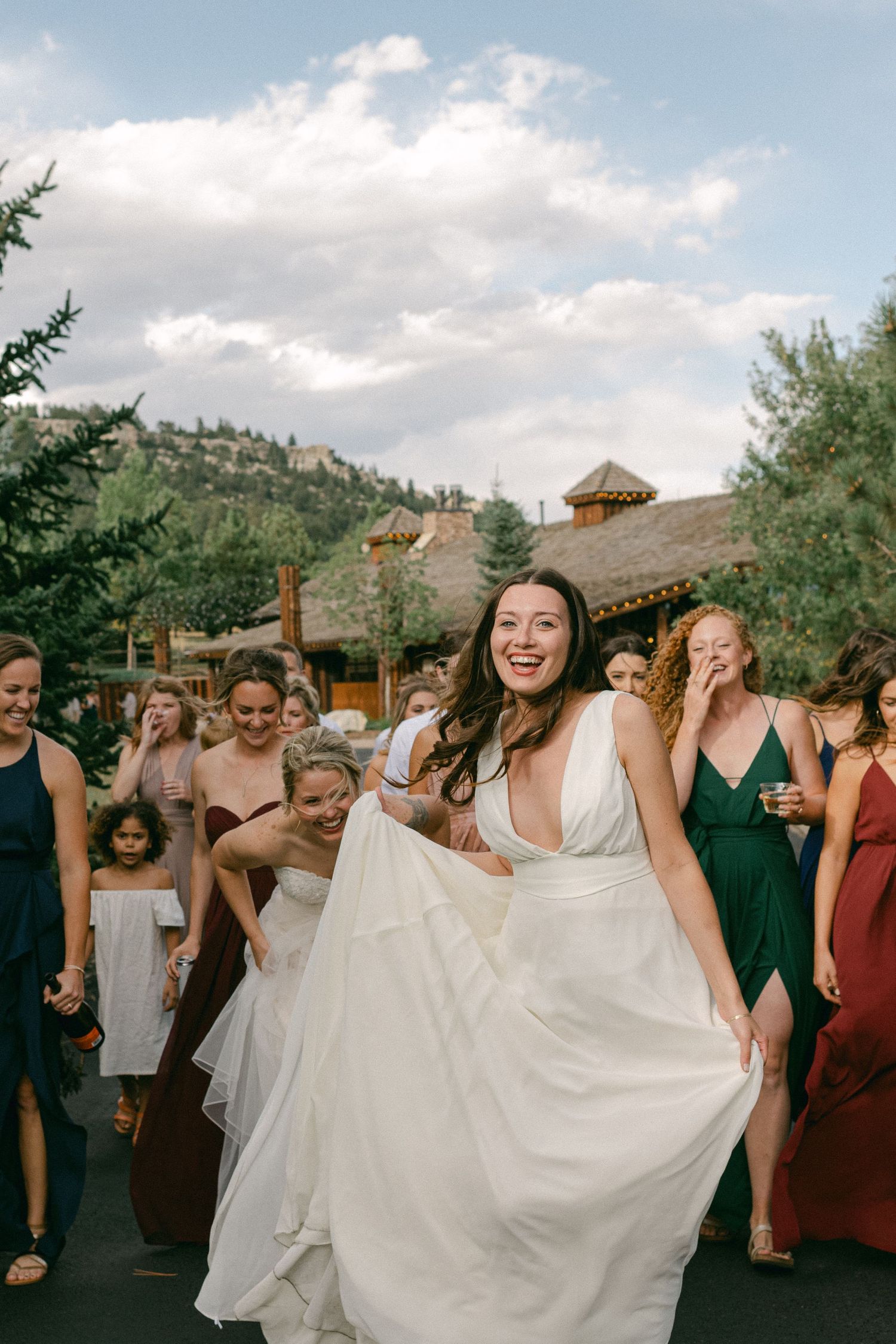 Person in flowing white wedding dress twirls joyfully outside rustic venue with mountain backdrop.