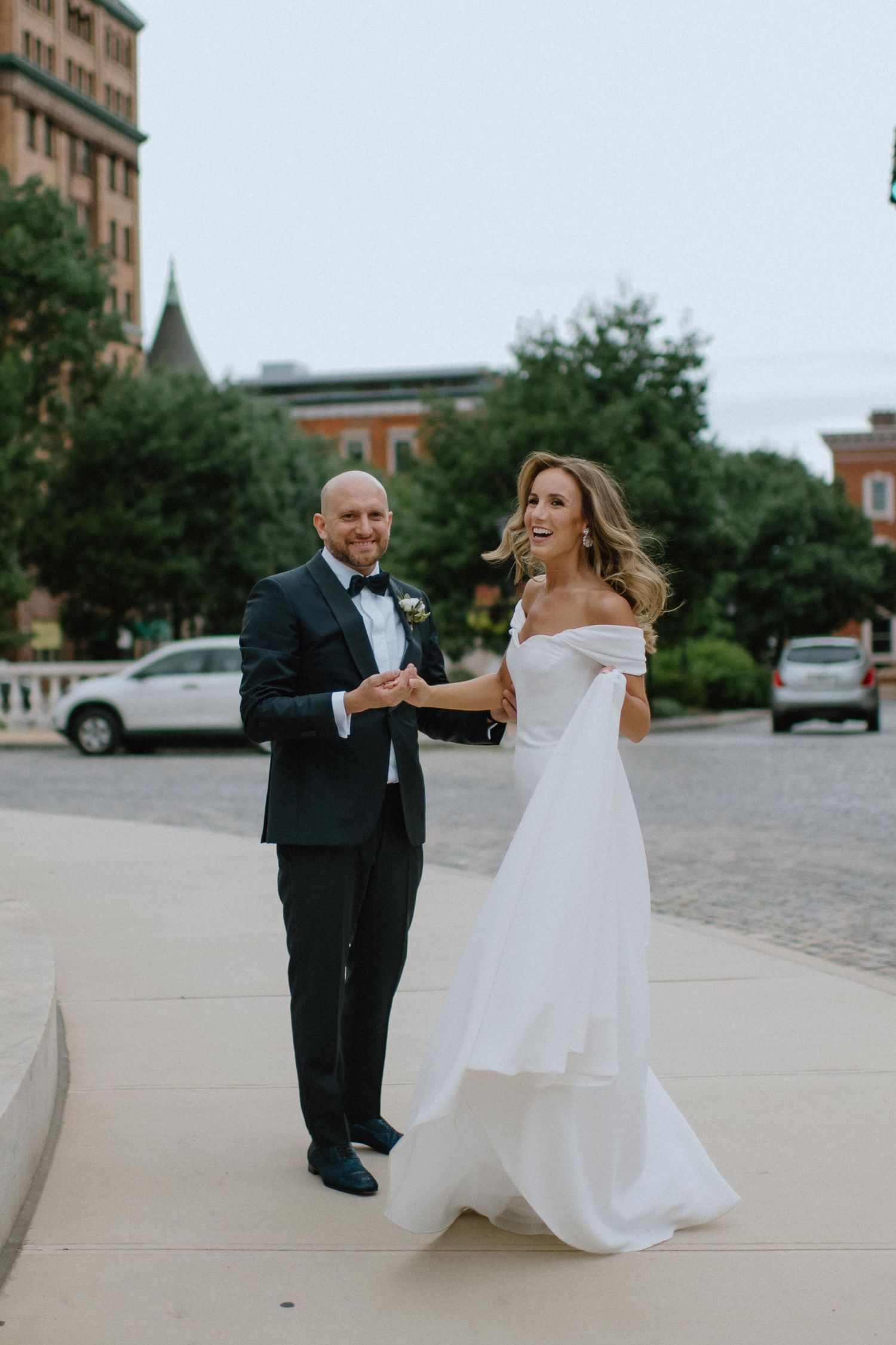 Couple dancing joyfully outside among urban architecture on their wedding day.