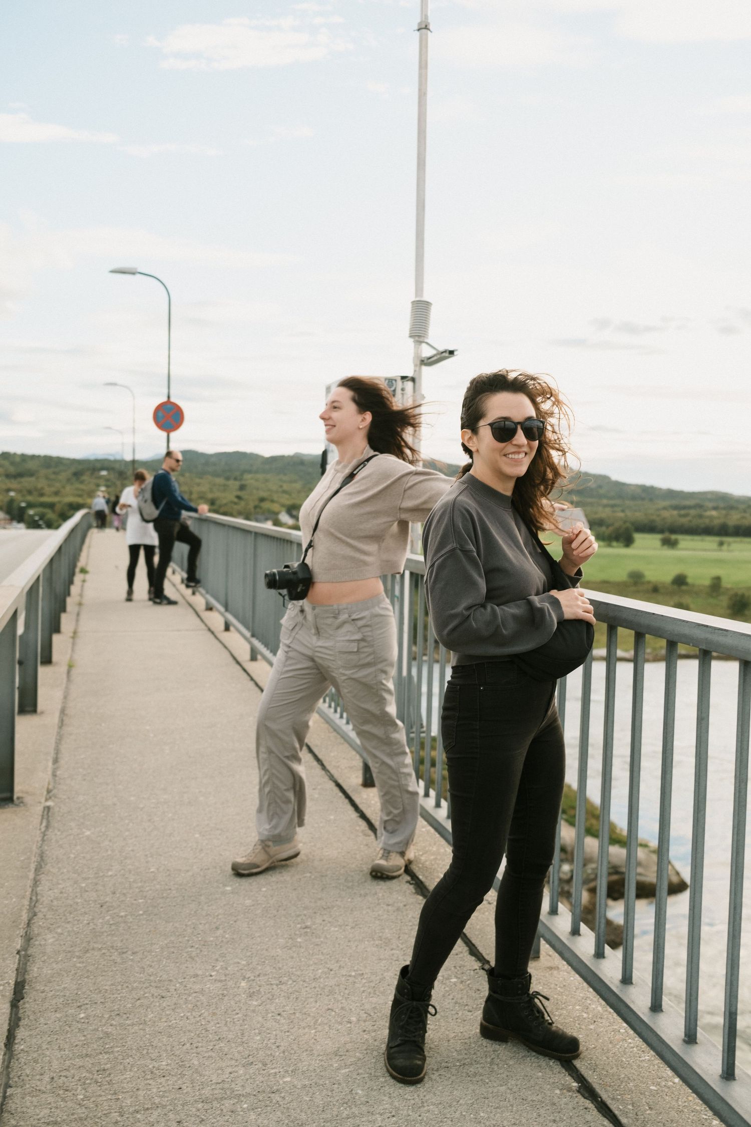 Friends posing and enjoying a windy day on a bridge walkway with countryside views.
