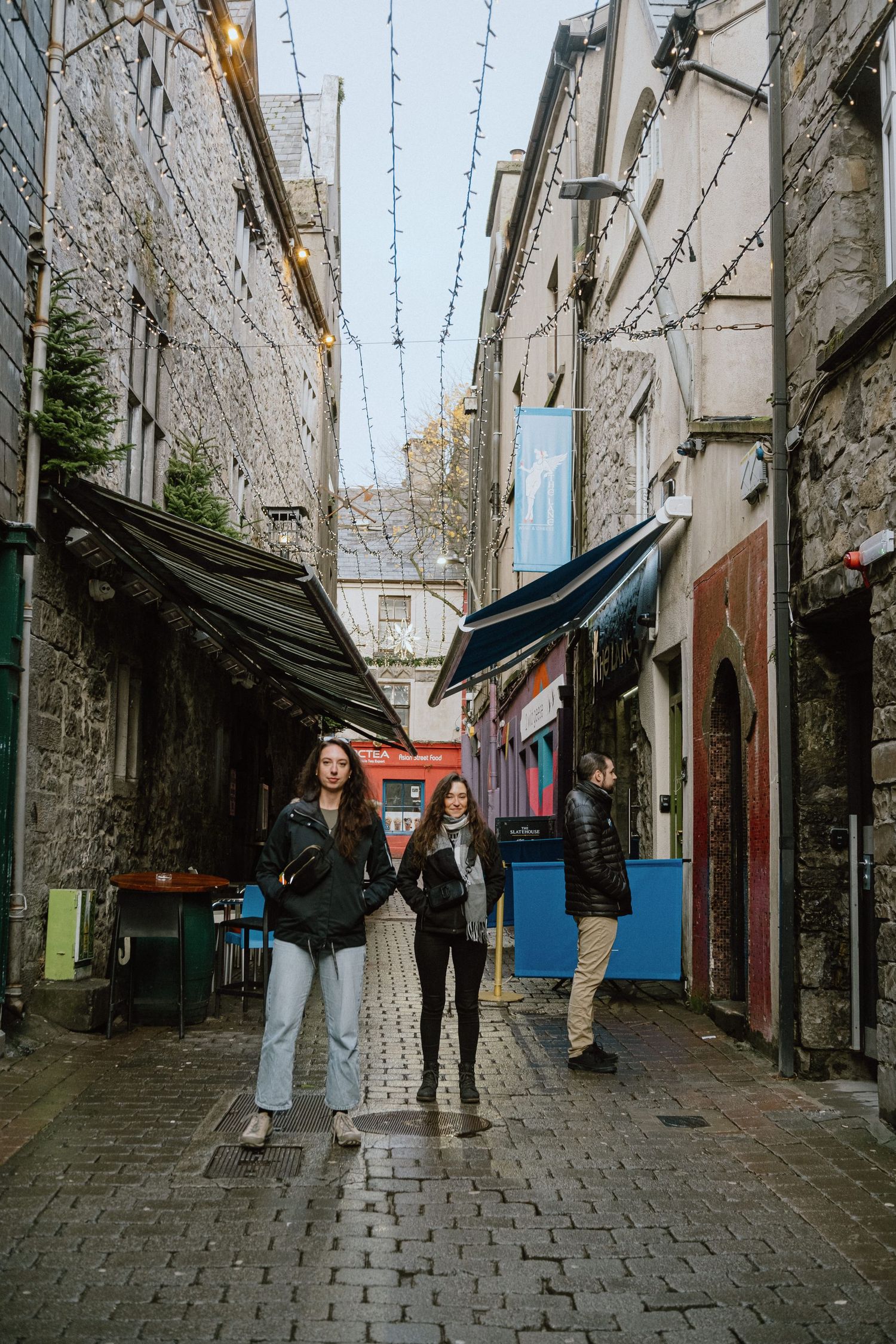 Narrow cobblestone street with string lights and stone buildings in Ireland.