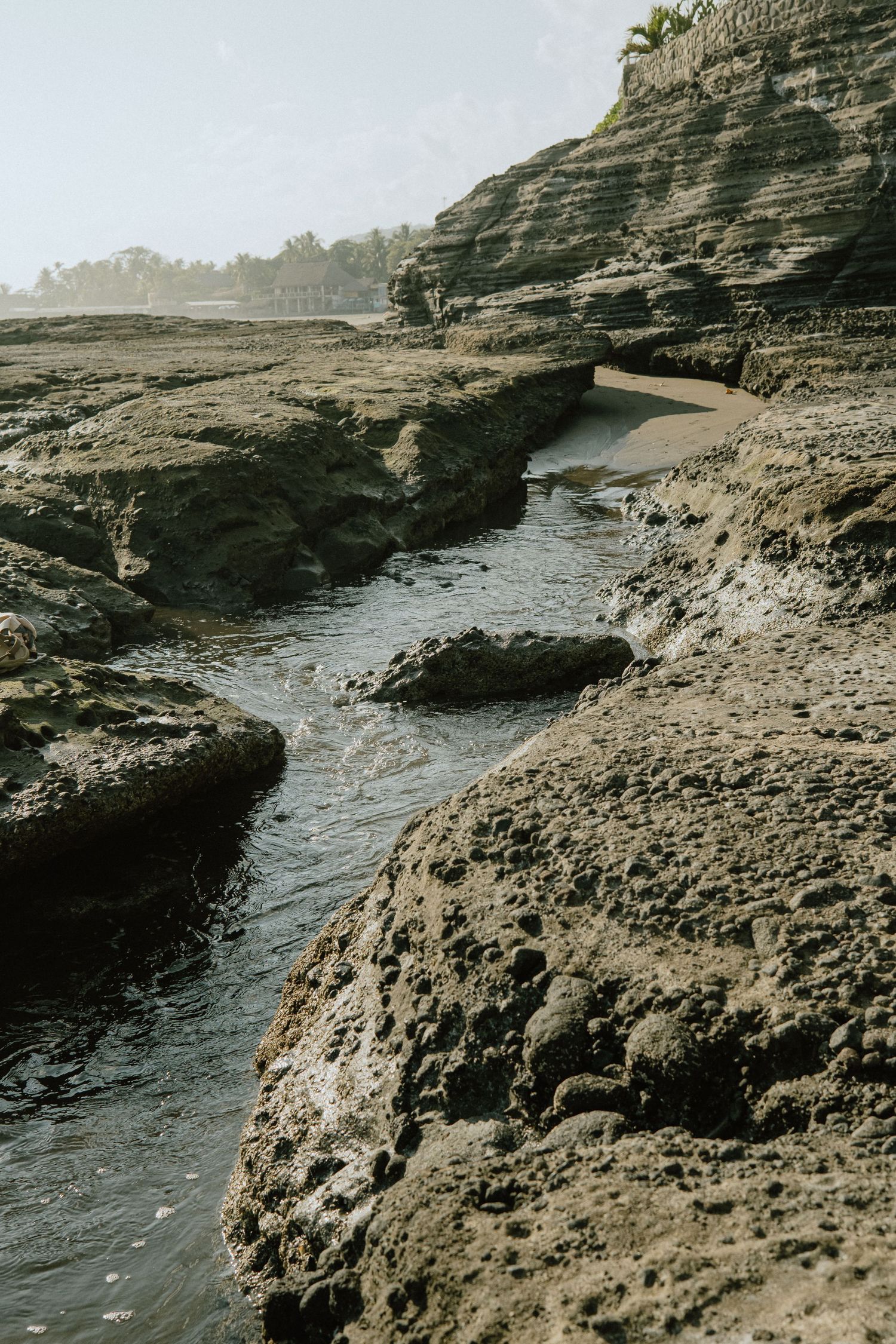 Rocky coastal terrain with winding water channel carved through layered sedimentary cliffs.