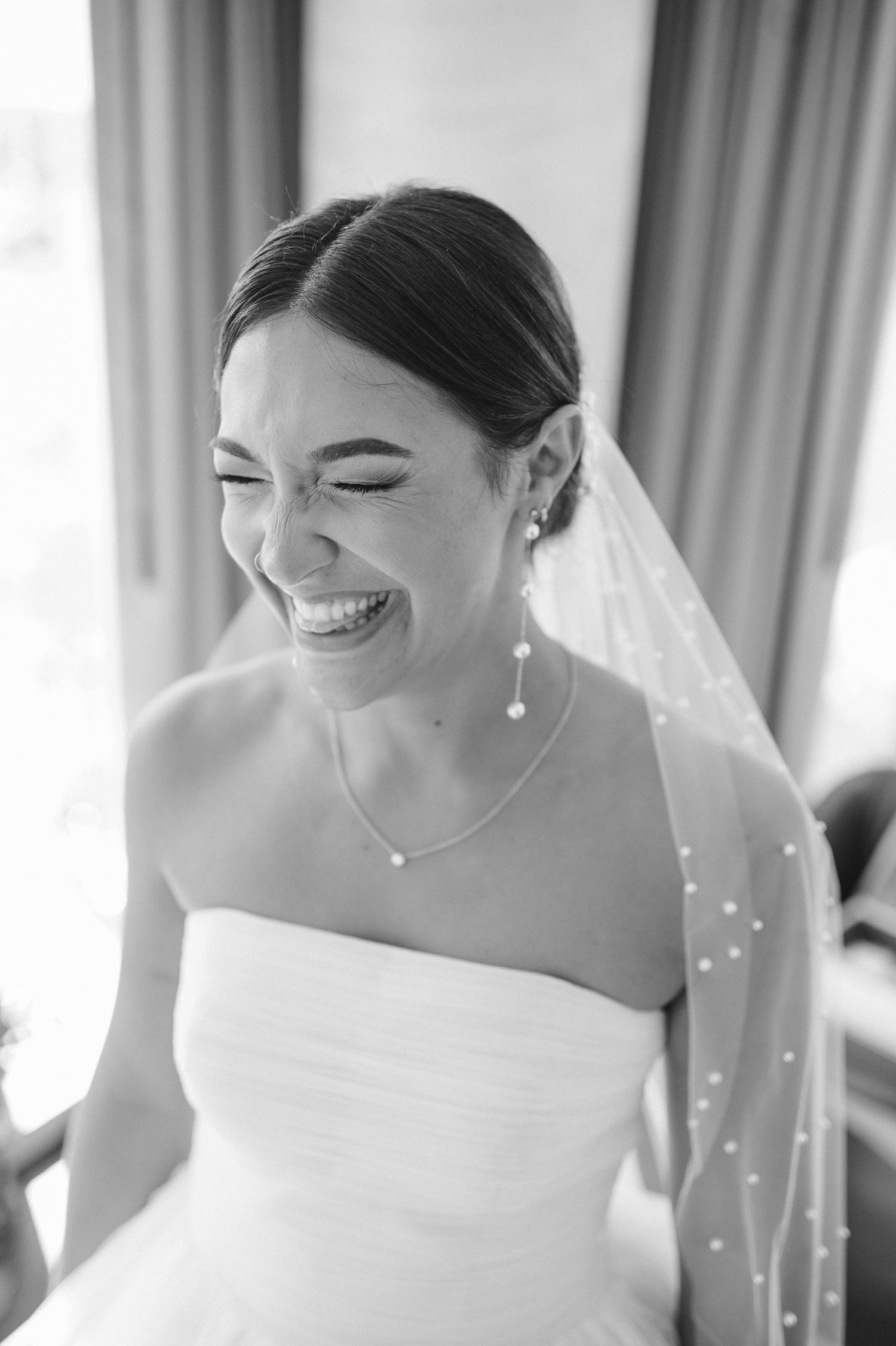 Black and white portrait of a joyful bride wearing a veil and strapless gown.