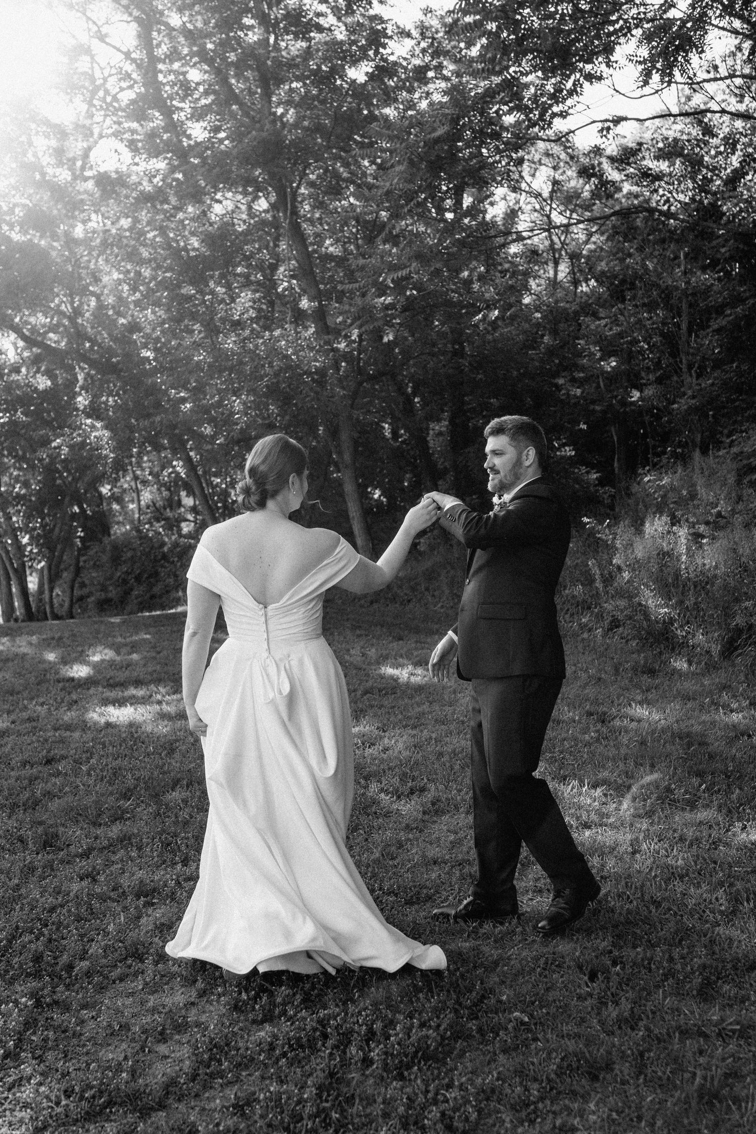 A couple dances together on a sunlit lawn during their wedding celebration.