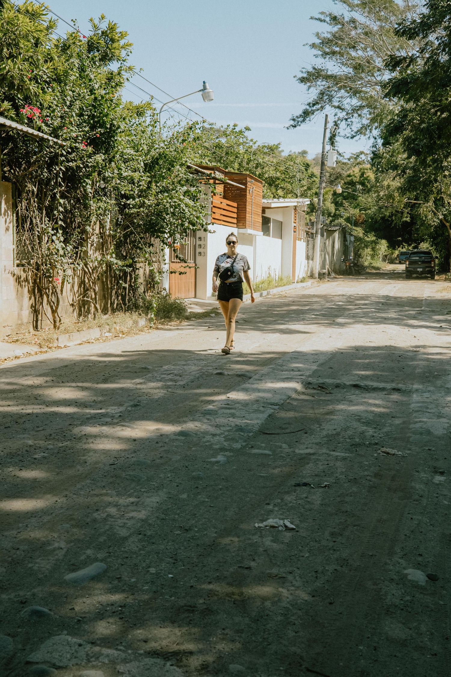 Person walking down a sunny suburban street with backpack.