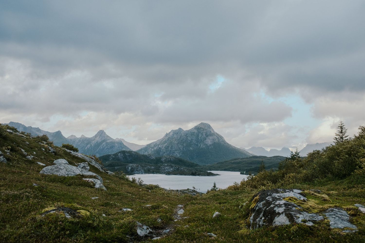 Rugged mountain peaks tower over a tranquil lake surrounded by rocky terrain and sparse vegetation.