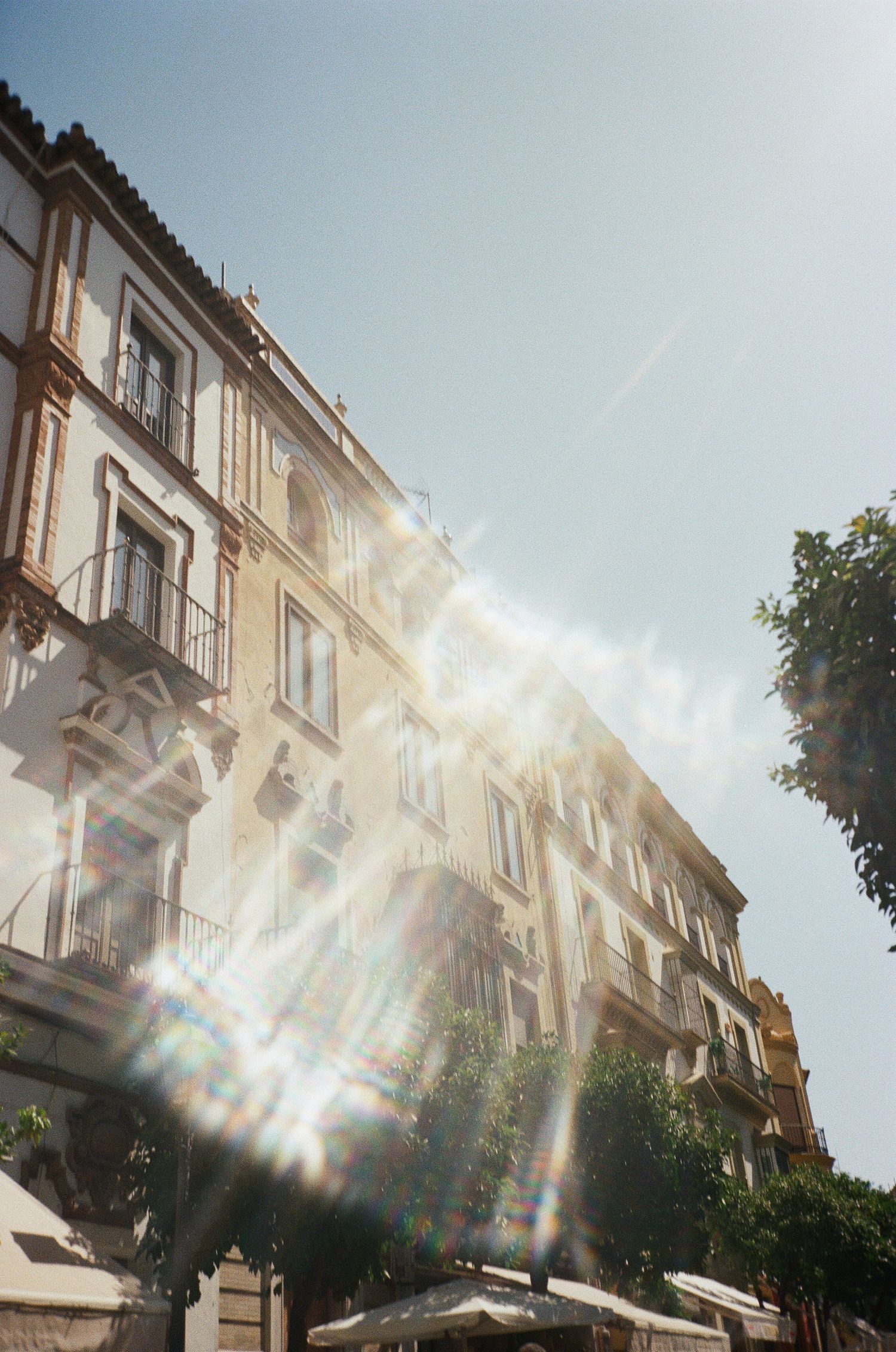 Sunlight streaming through buildings creating dramatic lens flares against a blue sky.
