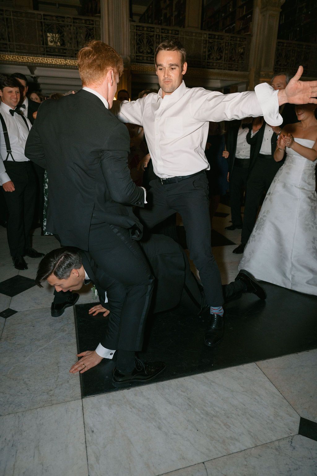 People performing a choreographed dance move on a marble floor at a formal event.