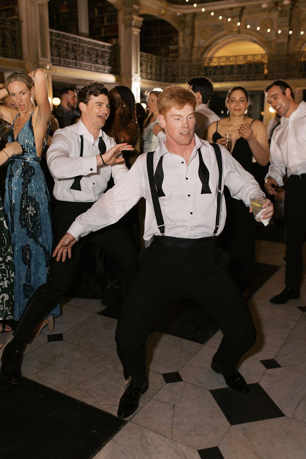 Men in suspenders performing choreographed dance moves at a wedding reception.