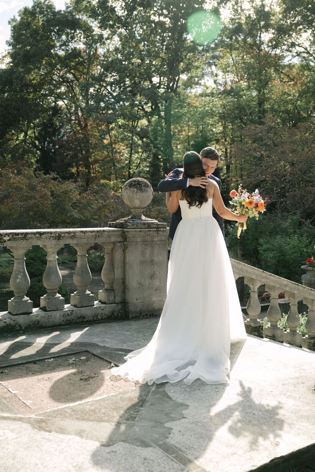 Wedding party members gather on a sunlit stone terrace with ornate balustrades.