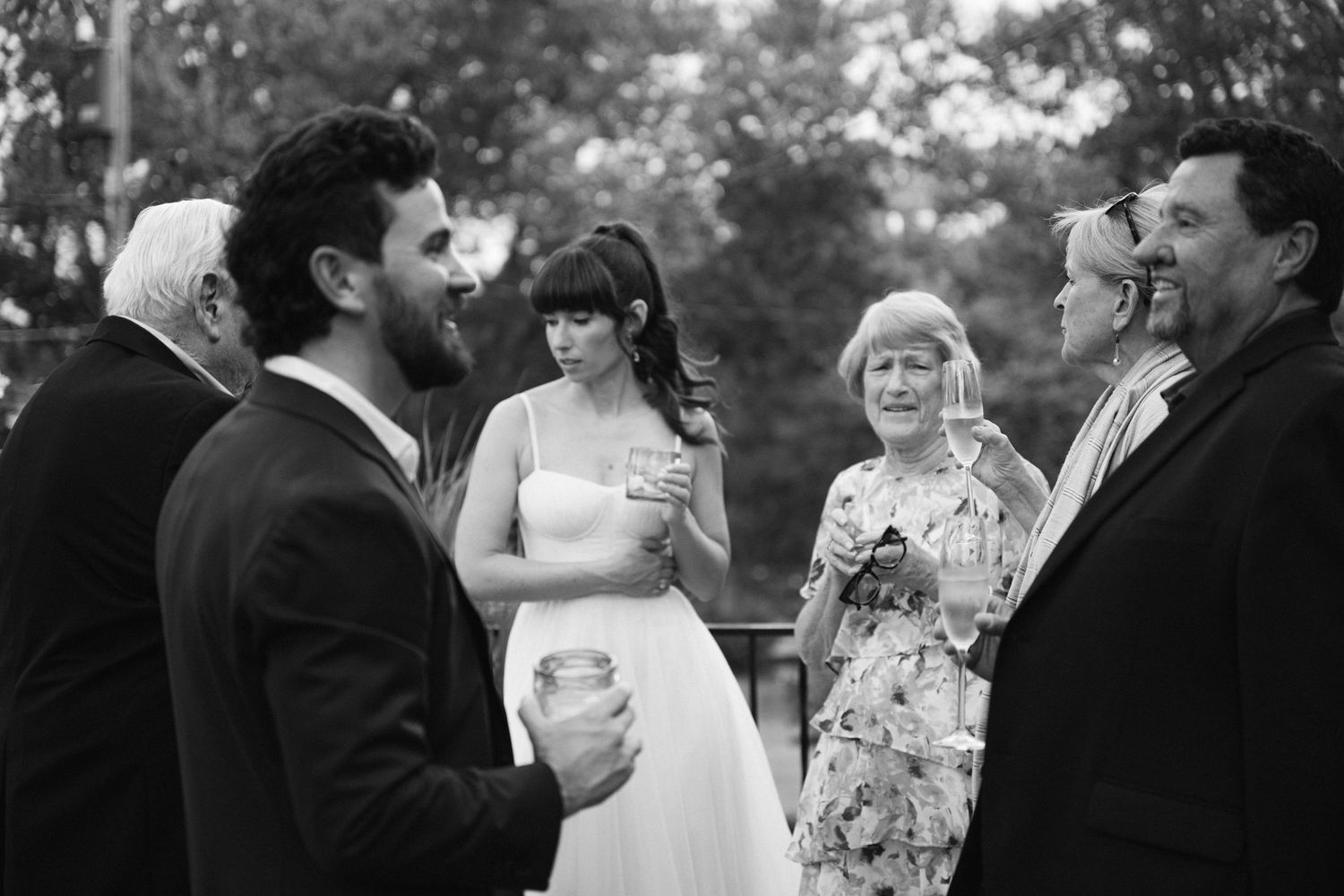 Wedding celebration outdoors with guests in formal attire gathered in a garden setting.