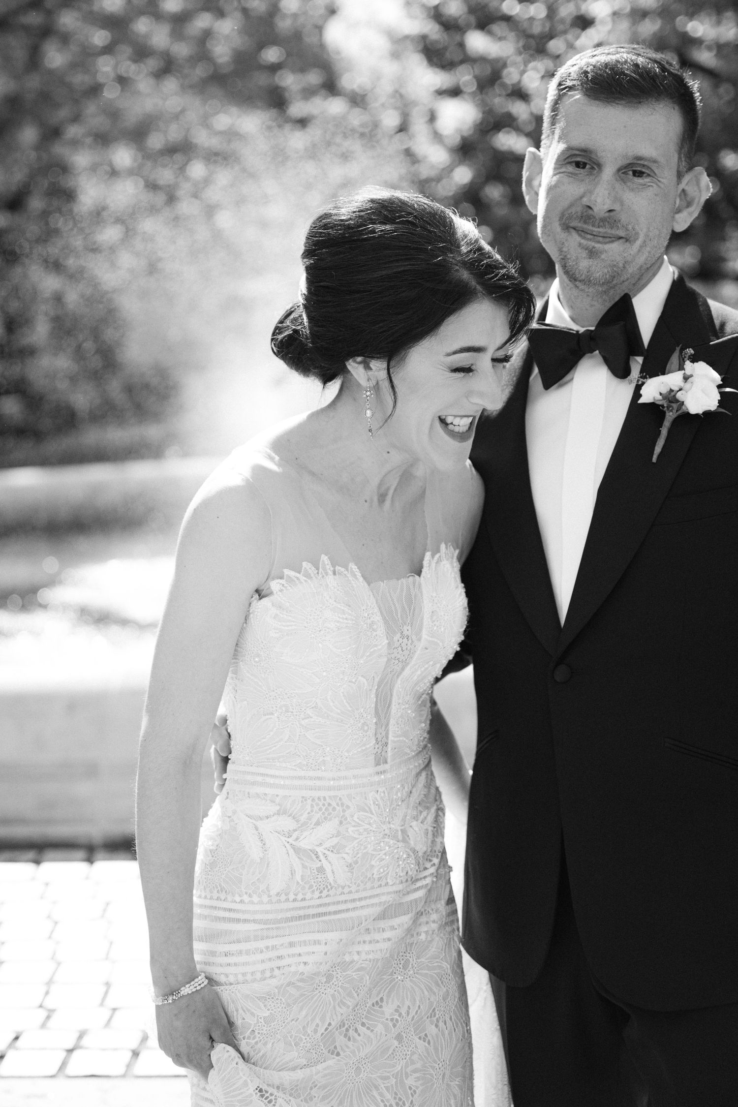 Black and white portrait of a newlywed couple sharing a joyful moment outdoors.