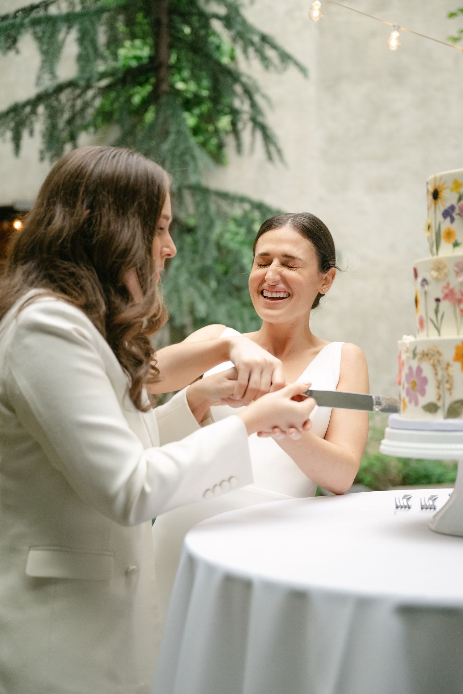 Two people share a joyful moment during an intimate conversation at a decorated table with twinkle lights in the background.