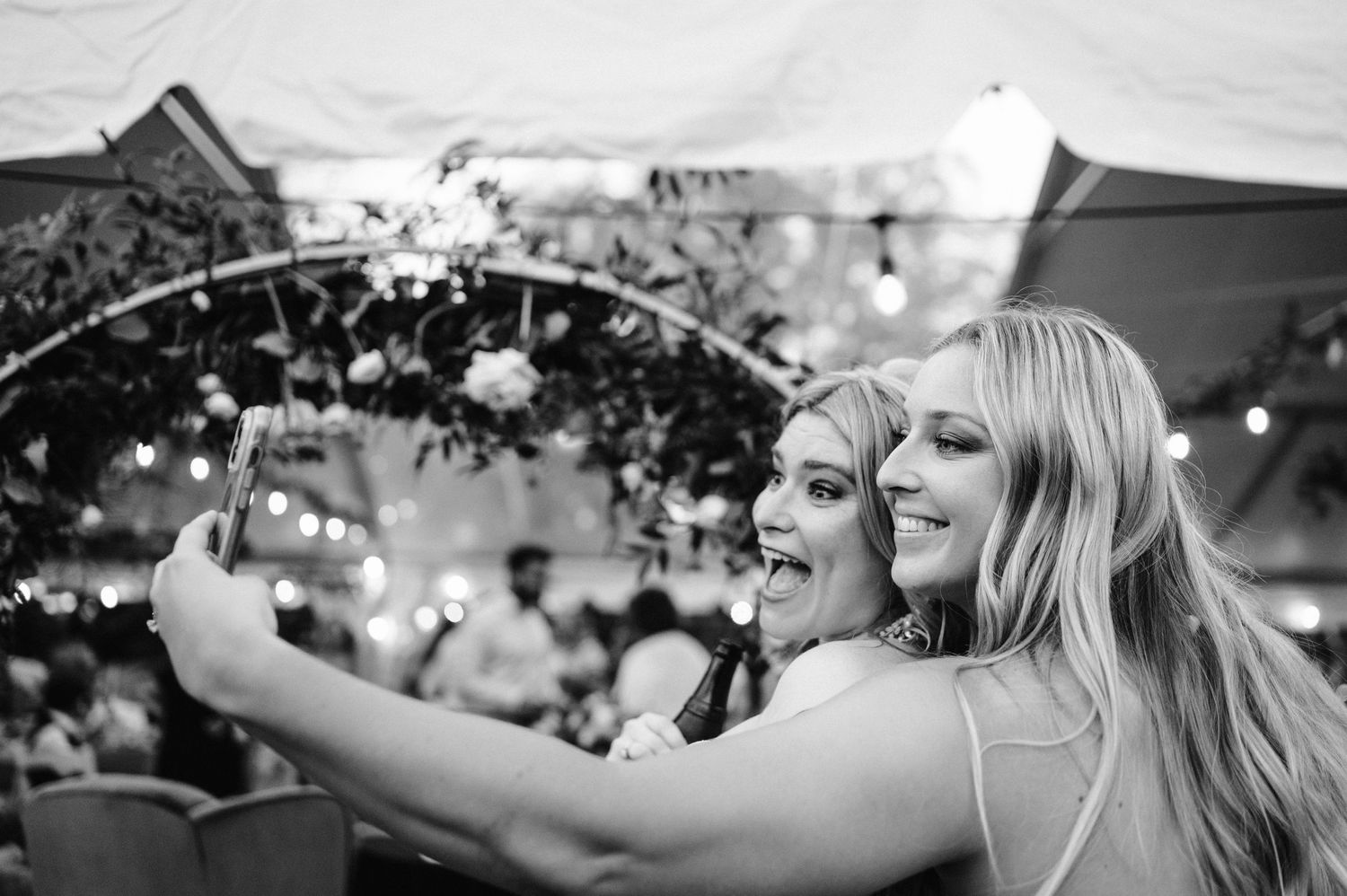 Two wedding guests taking a selfie together during an outdoor celebration.