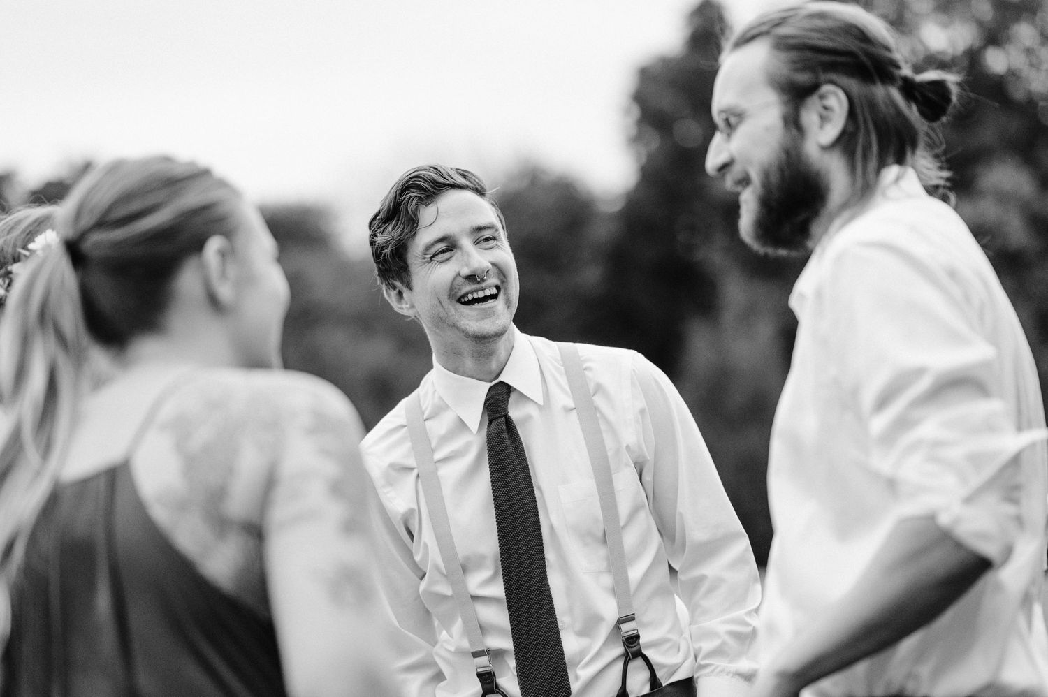 Black and white candid photo of guests sharing laughs during outdoor wedding reception.