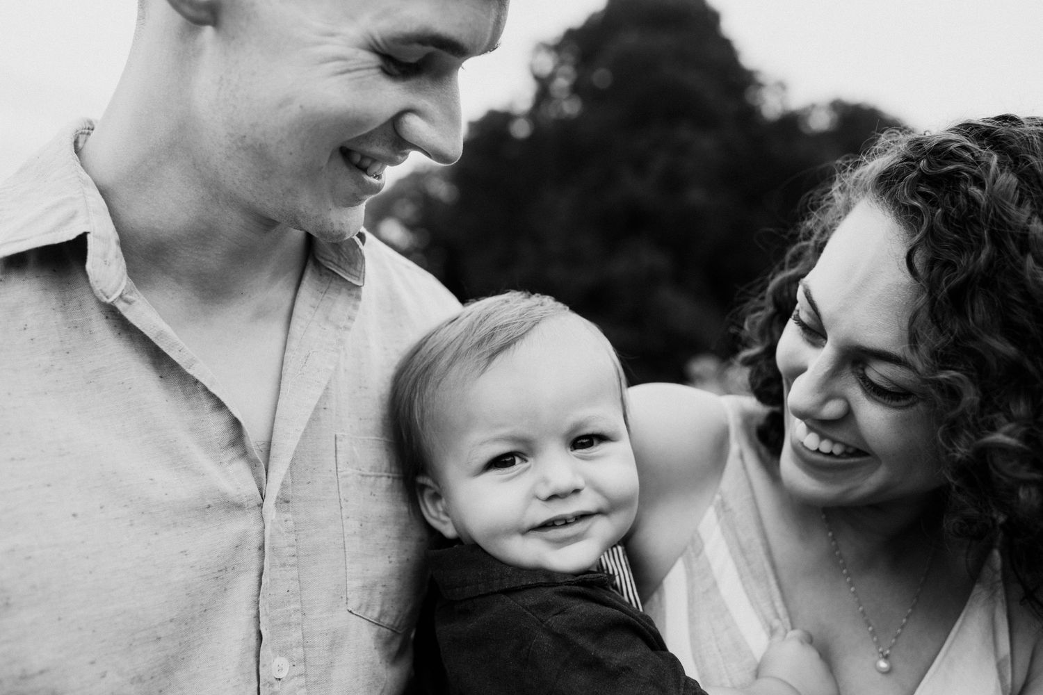 Black and white candid photo of a small family smiling together outdoors.