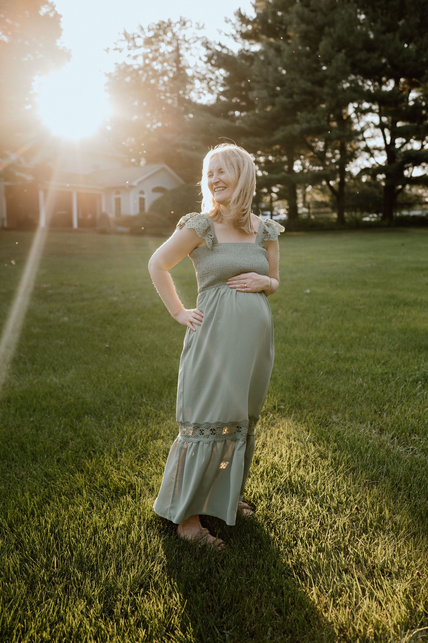 Woman in flowing sage dress poses on lawn during sunset with house in background.