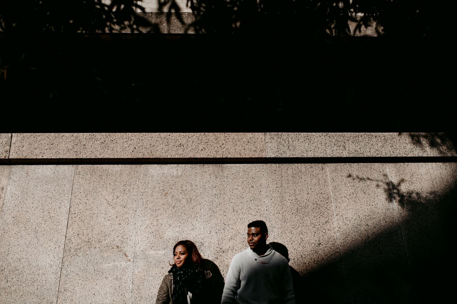 A stylistic overhead shot of a couple walking in shadow against a concrete wall.