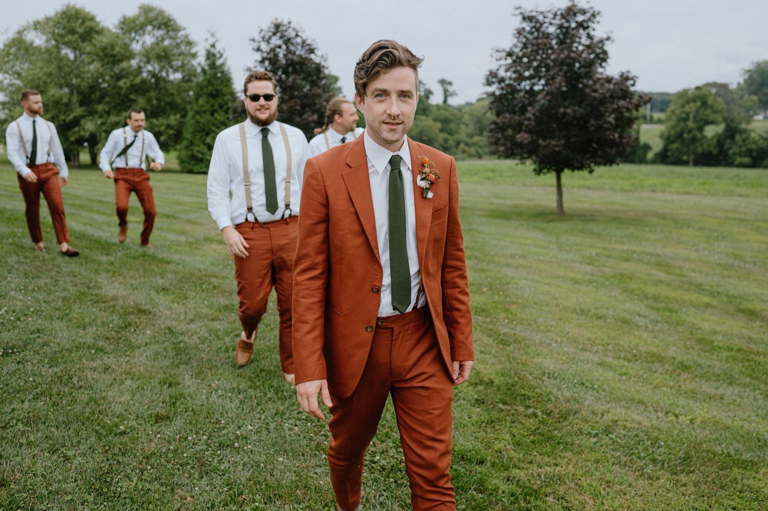 groom and groomsmen walking in orange suits at backyard wedding