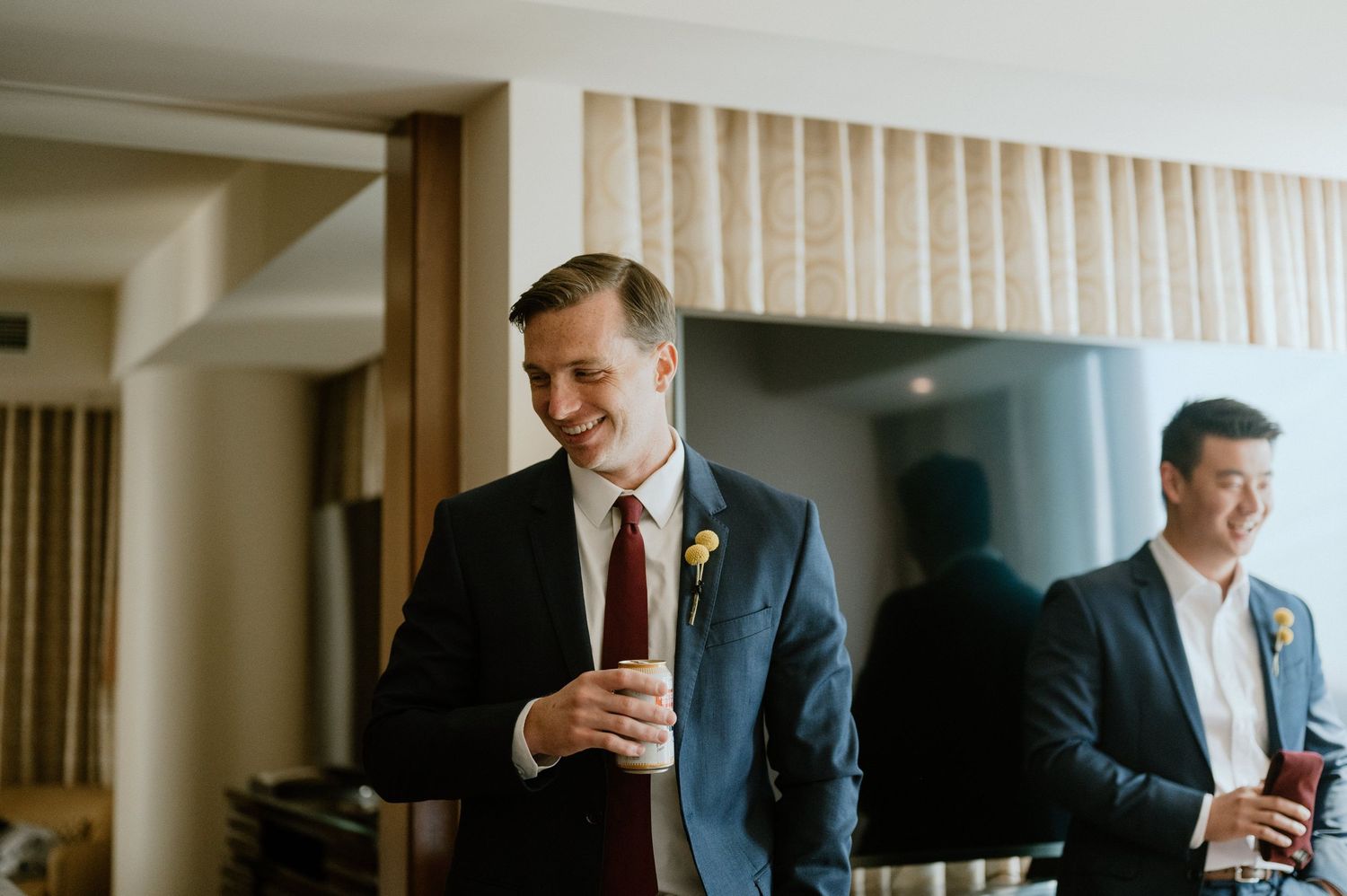 Wedding party members in suits prepare for ceremony in hotel room.