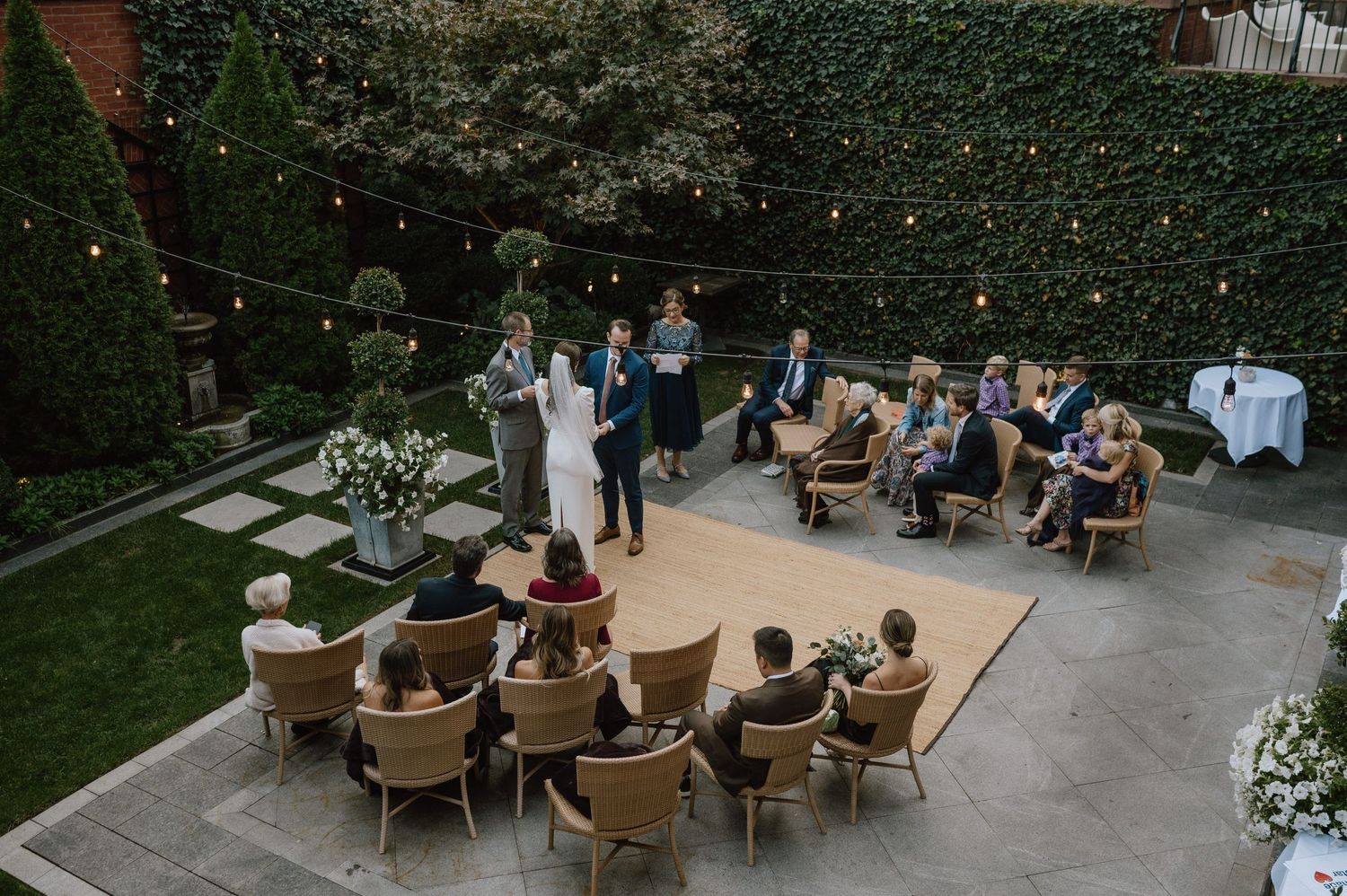 Aerial view of an intimate outdoor wedding ceremony with guests seated in wicker chairs on a patio.