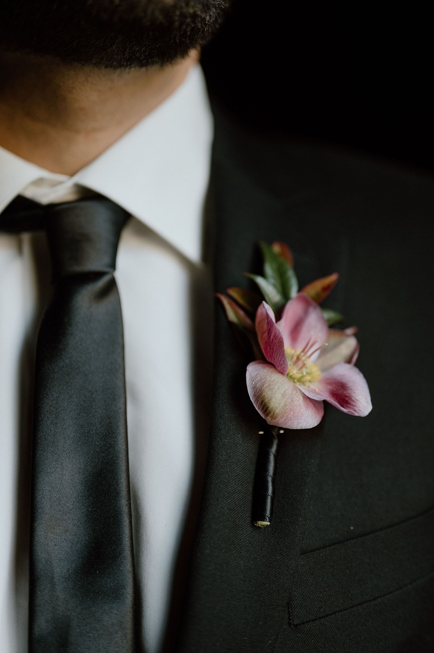 Close-up of a pink lily boutonniere pinned to a dark suit lapel.