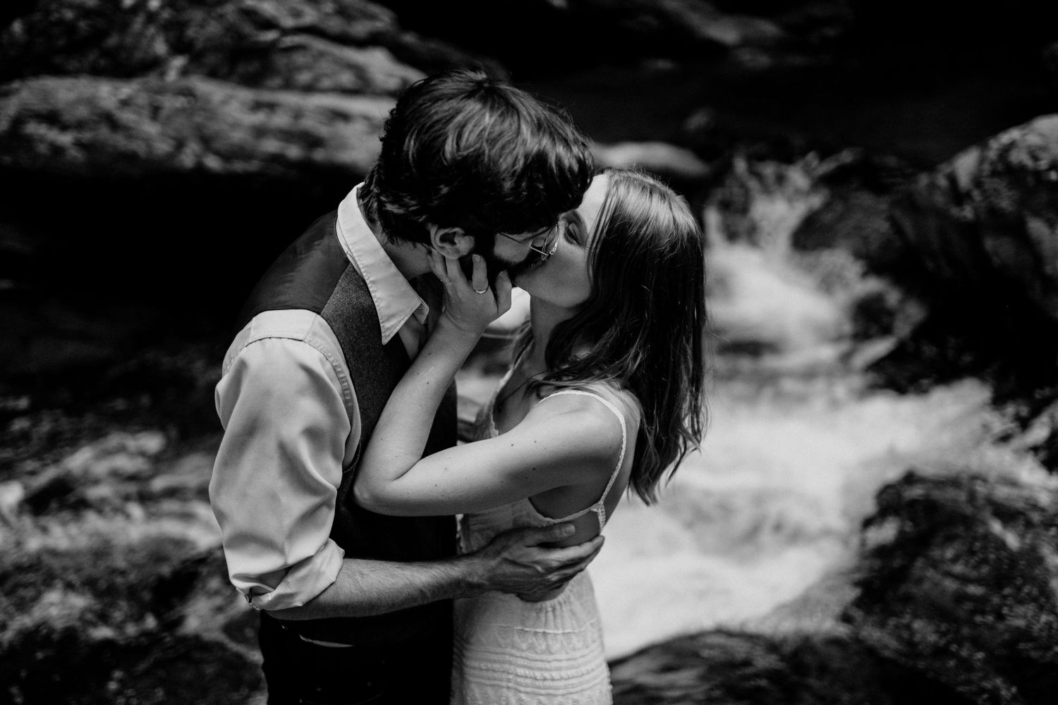 Intimate black and white portrait of newlyweds embracing by a waterfall.