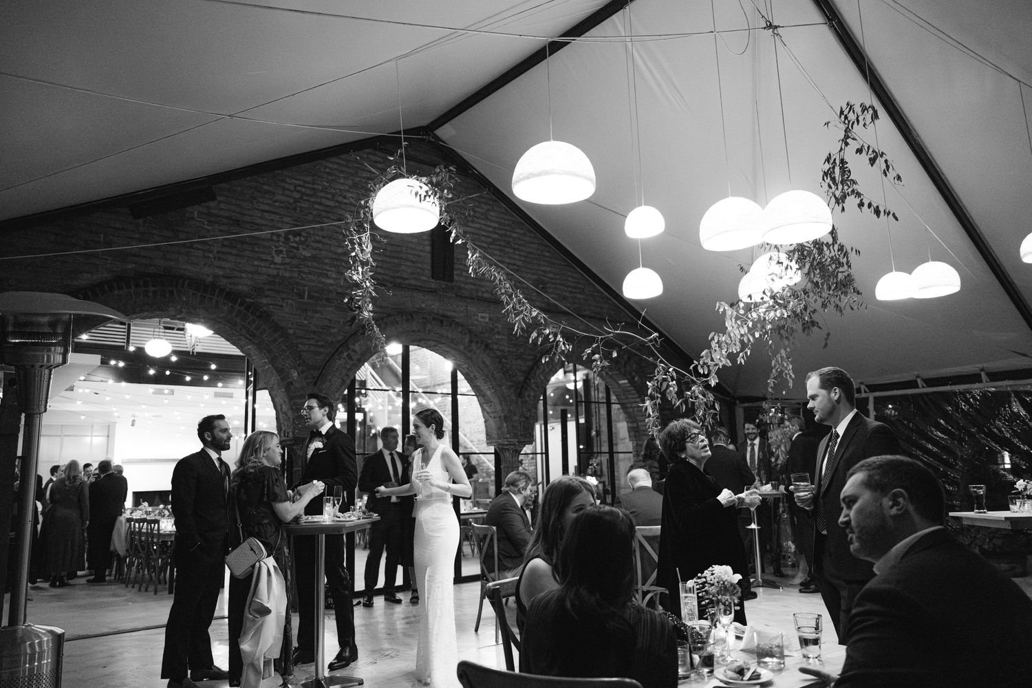 Black and white photo of a reception venue decorated with hanging globe lights and greenery.
