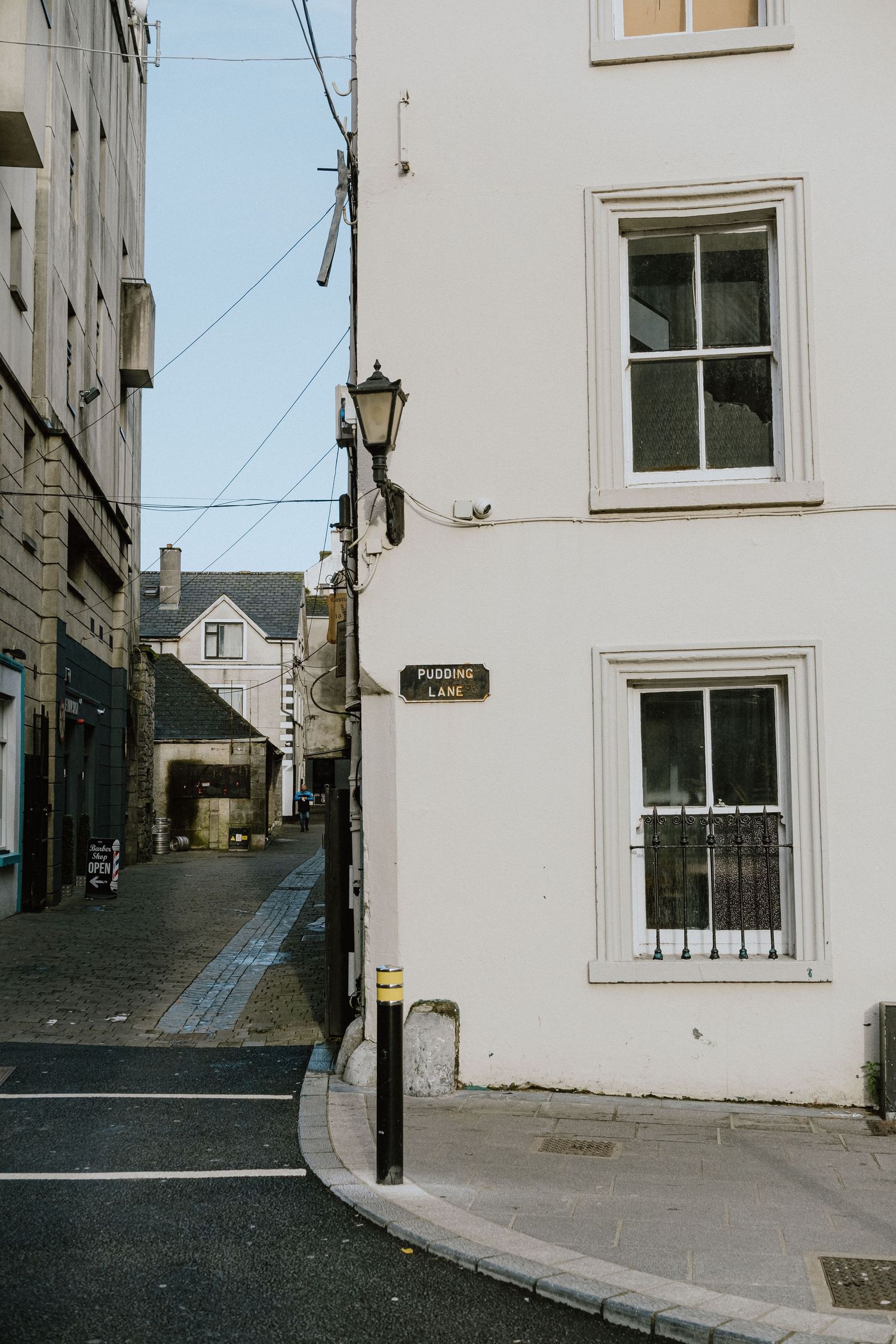 Narrow cobblestone alley between white buildings with traditional street lamps.