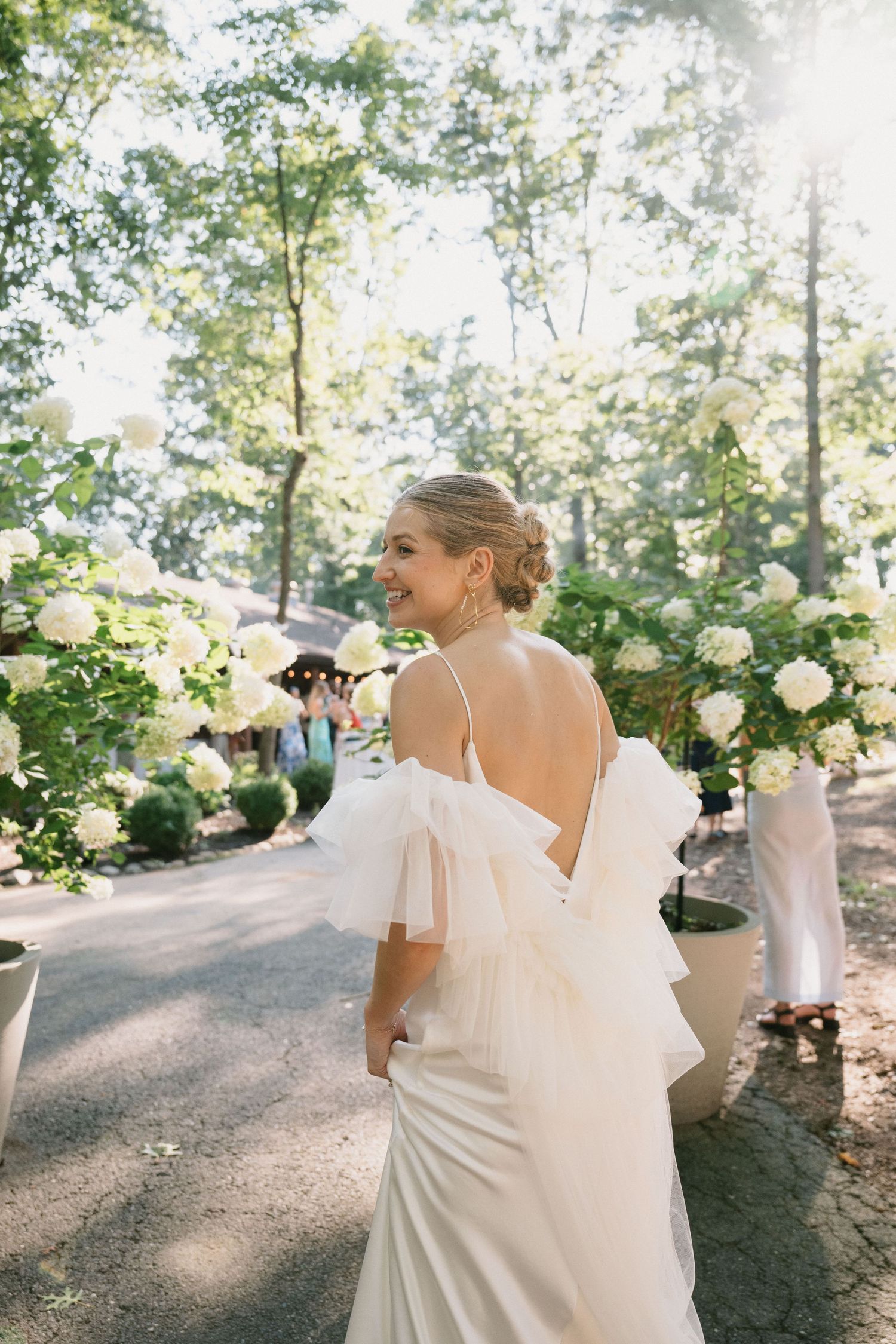 A bride in an elegant white dress stands among blooming roses in a garden setting.