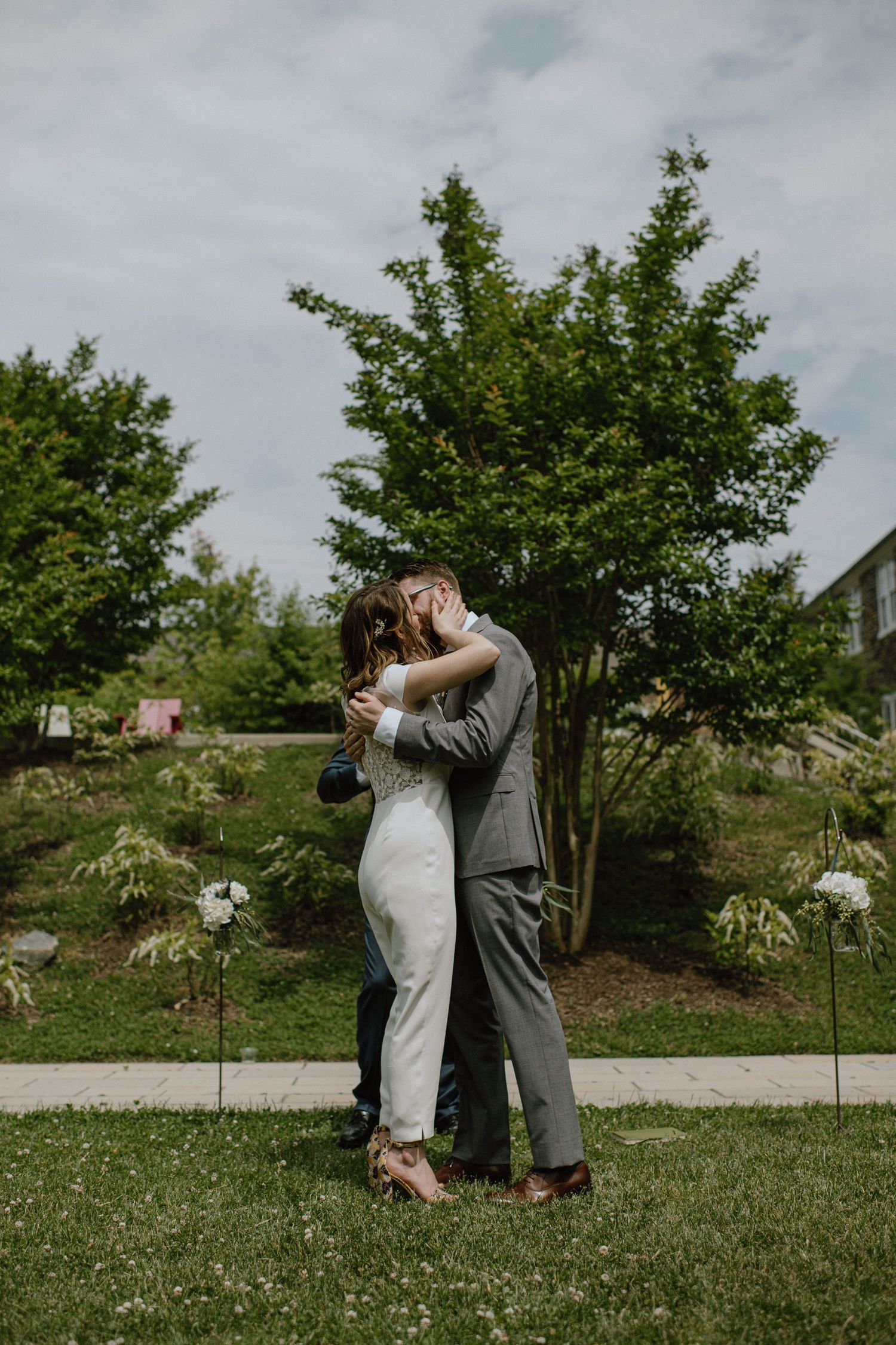 A romantic outdoor wedding moment captured beneath lush green trees.