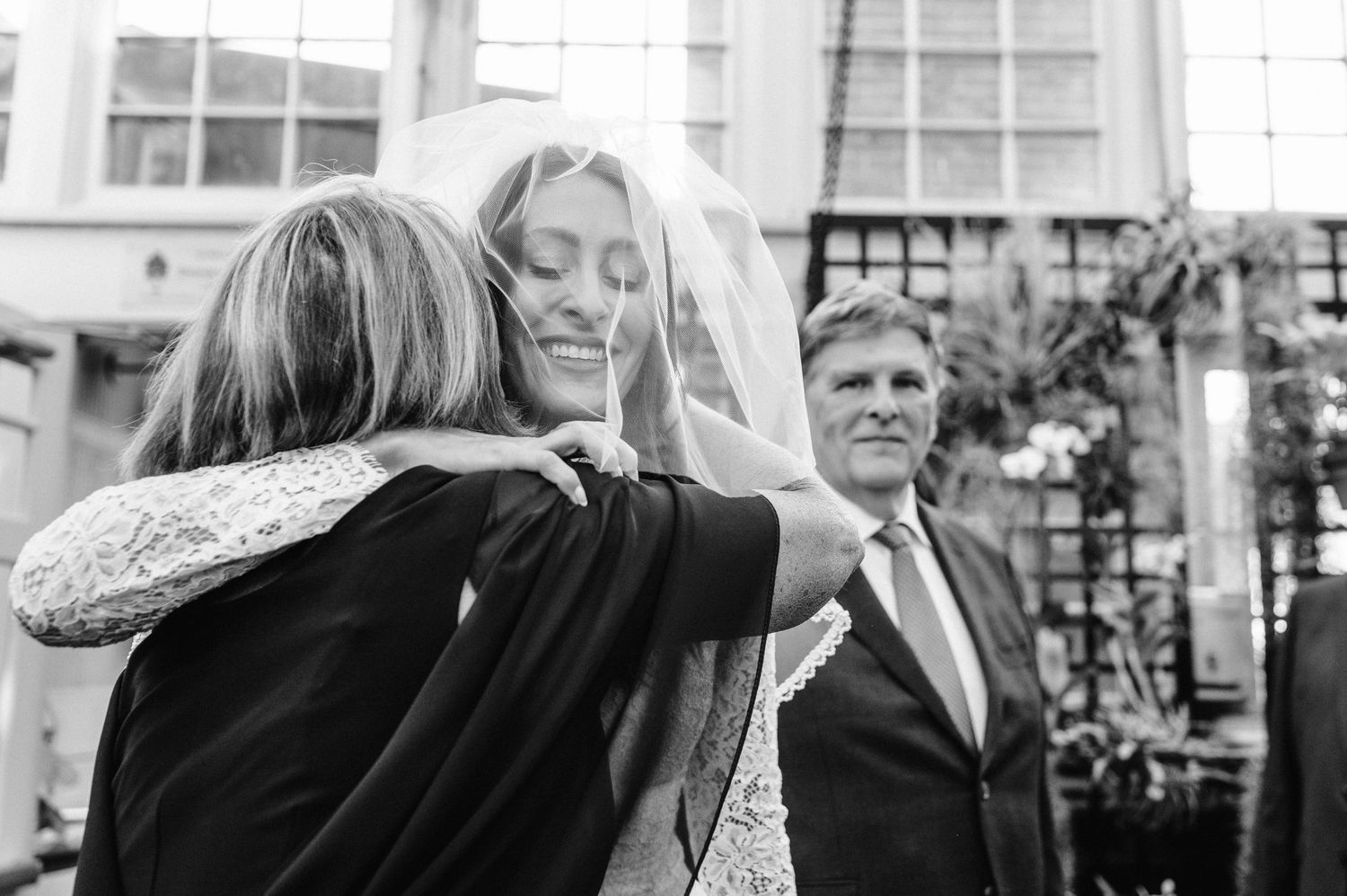 An emotional embrace during a wedding ceremony in a glass-roofed venue.
