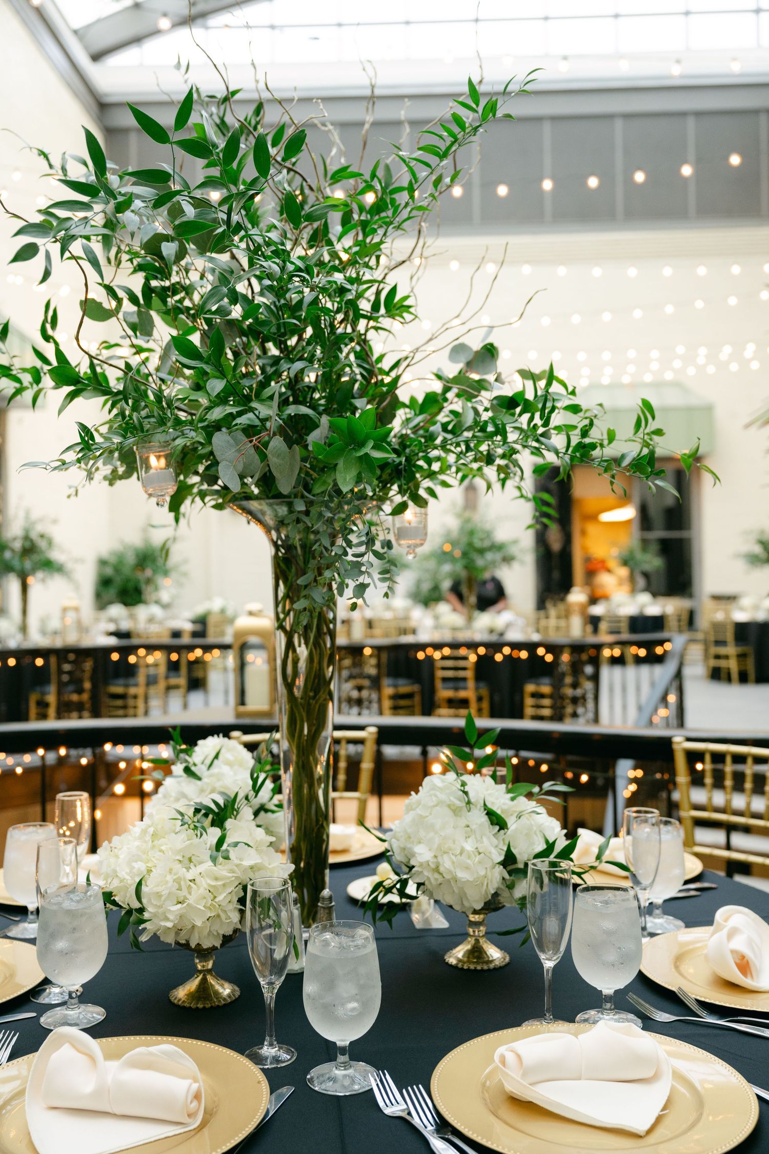 Elegant table settings with white floral centerpieces and greenery at a wedding reception.