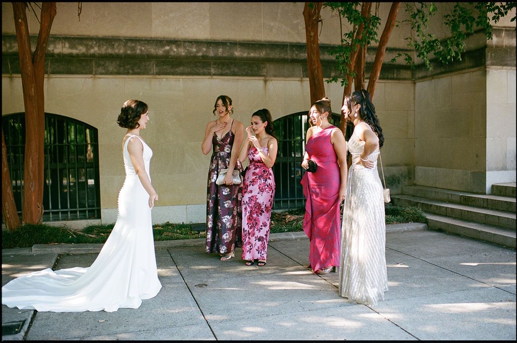 A bride in a white wedding gown poses with bridesmaids in pink dresses during an outdoor photo session.