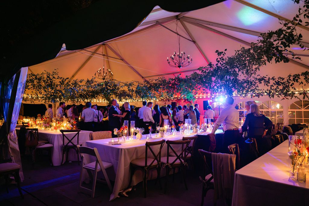 Wedding reception tent illuminated with colorful lights and string lighting creating a magical atmosphere.