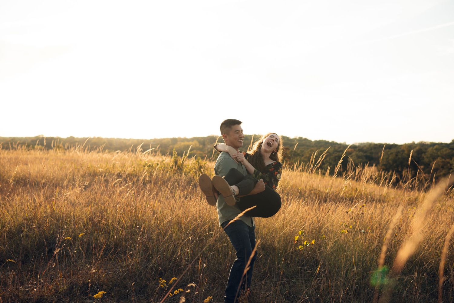 Silhouettes of couple walking through tall grass field at dusk.