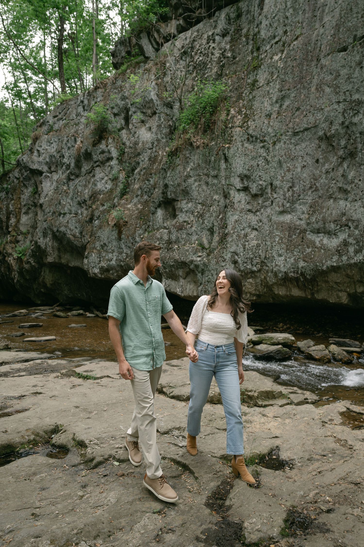 Couple exploring rocky terrain near a cliff wall in casual summer attire.