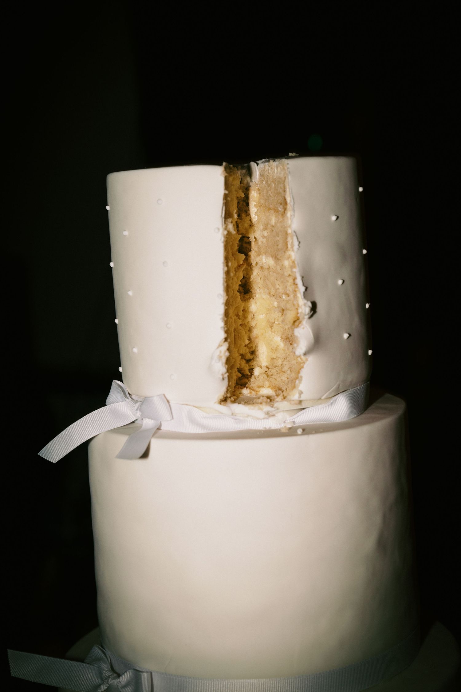 A classic white two-tier wedding cake with a slice removed showing the golden interior layers.
