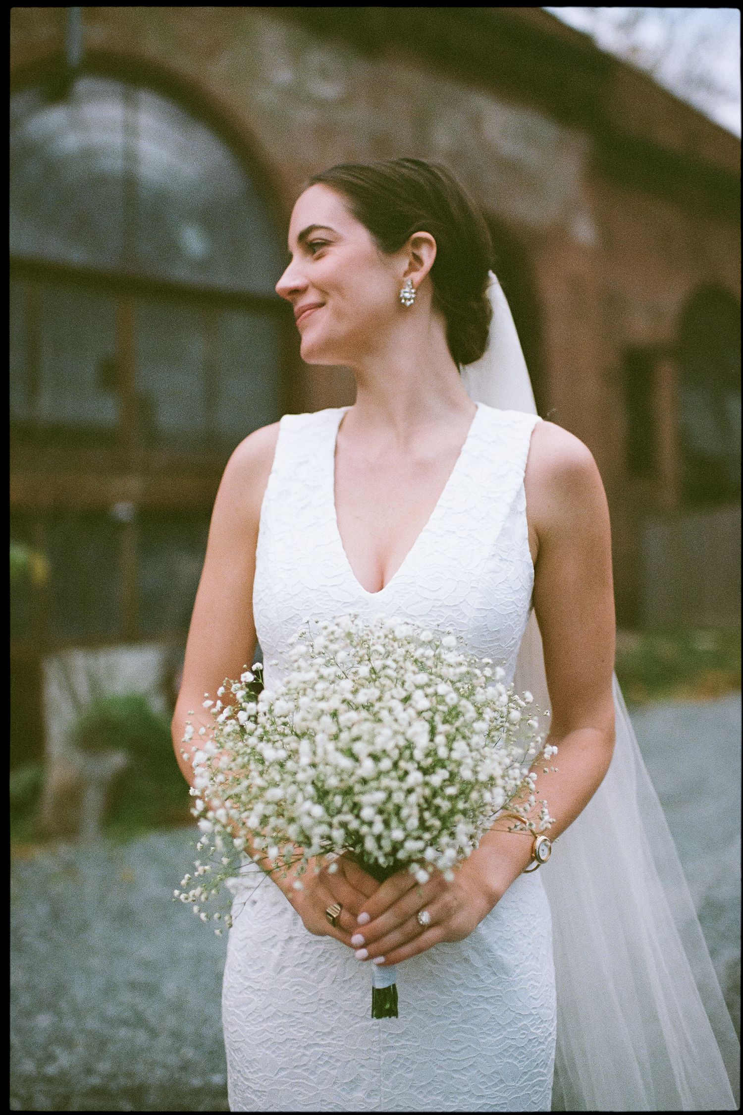 Elegant bride in a fitted white dress holding a delicate baby's breath bouquet while posing outdoors.