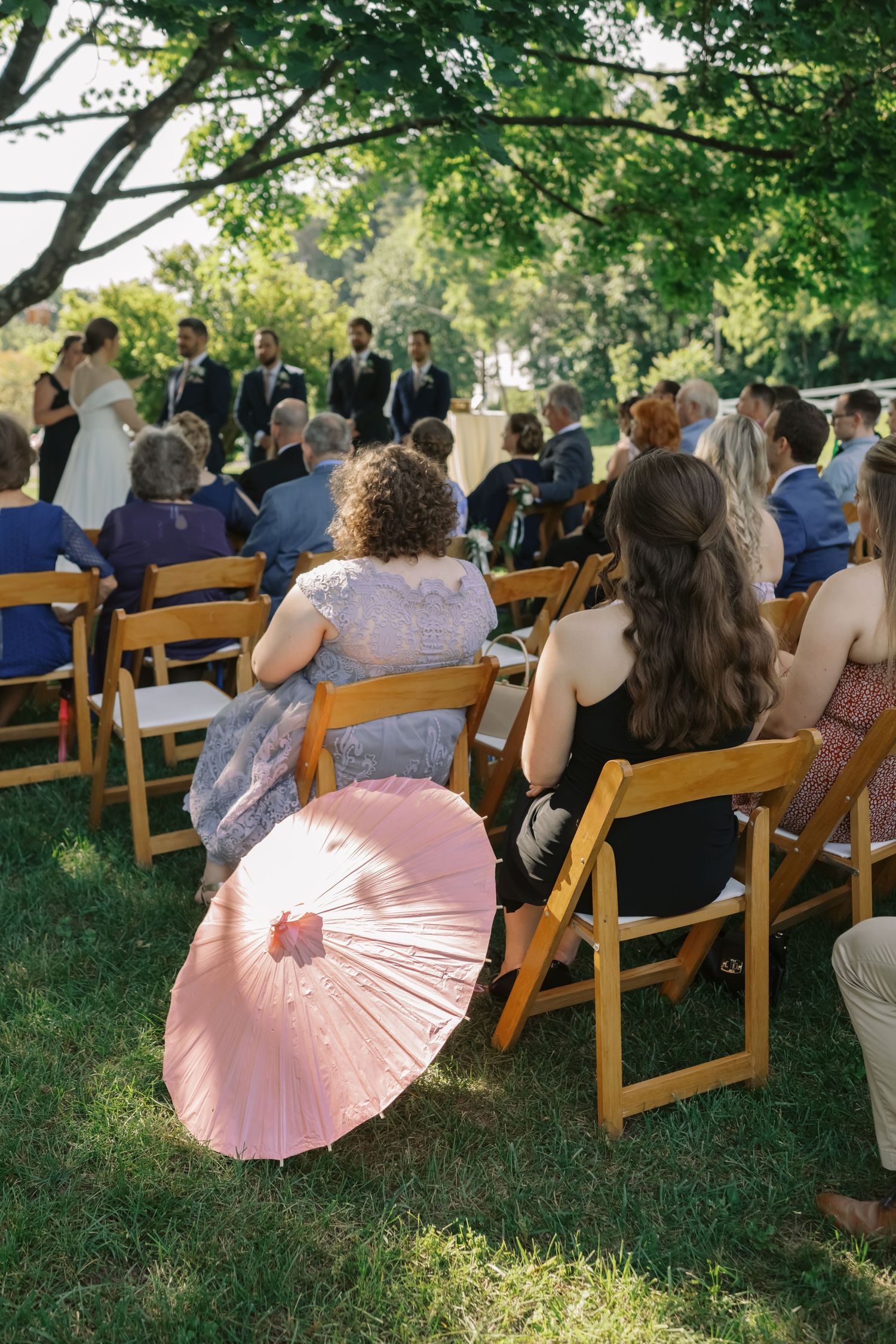 Couple exchanging rings during outdoor wedding ceremony under large tree.