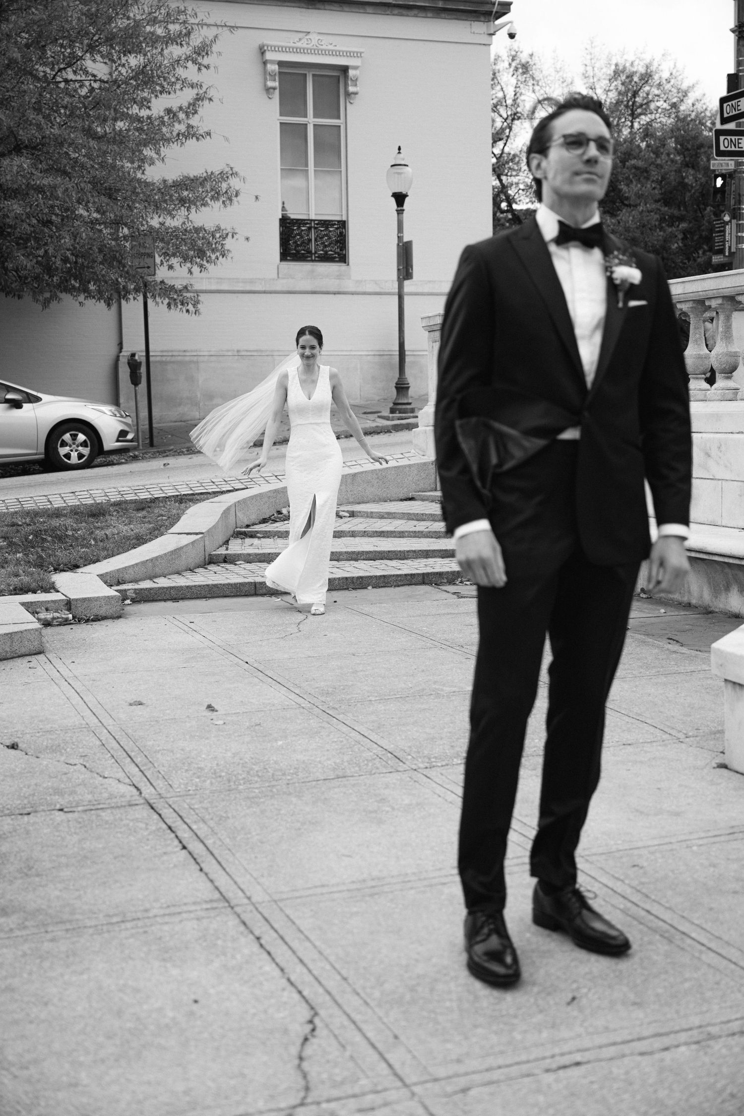 Black and white wedding photo showing playful moment with couple on city sidewalk and steps.