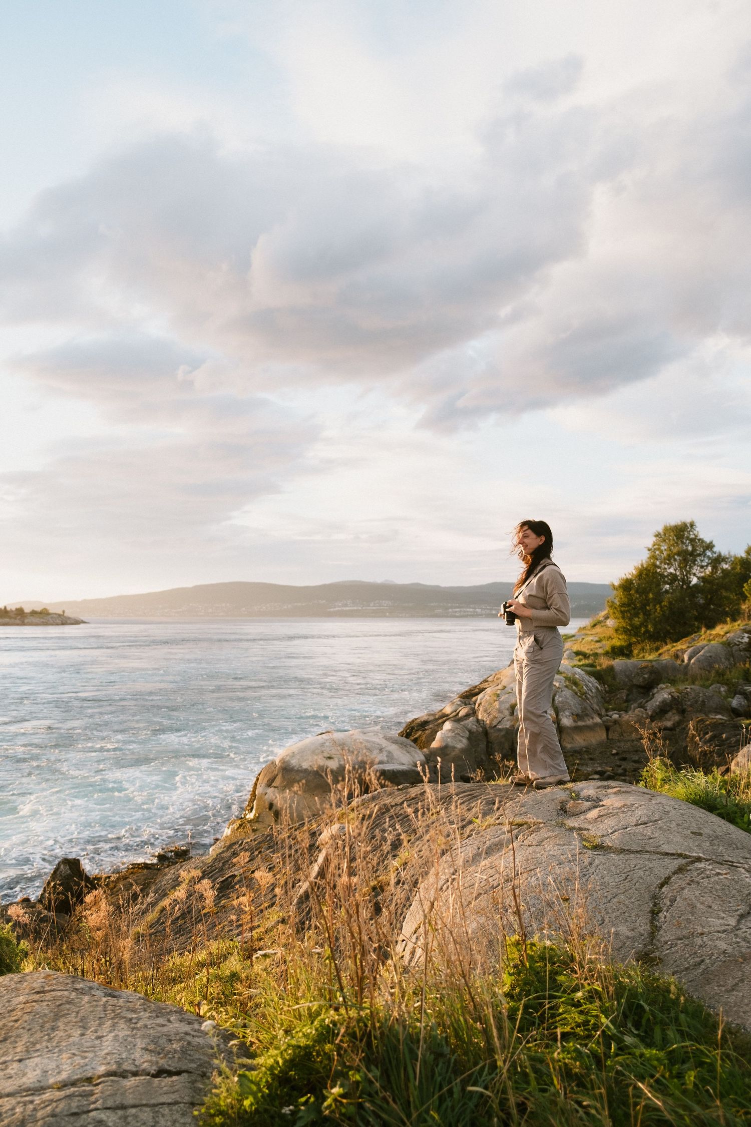 Coastal landscape with figure standing on rocky cliff overlooking ocean at sunset.