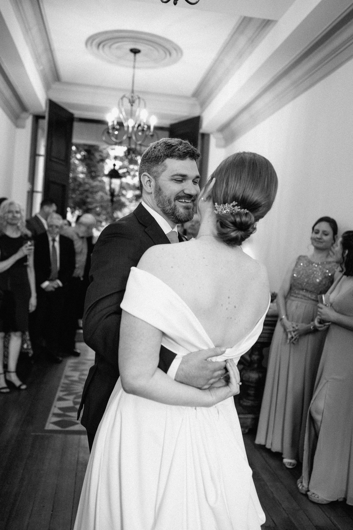 Intimate black and white portrait of a couple's first dance with guests looking on.