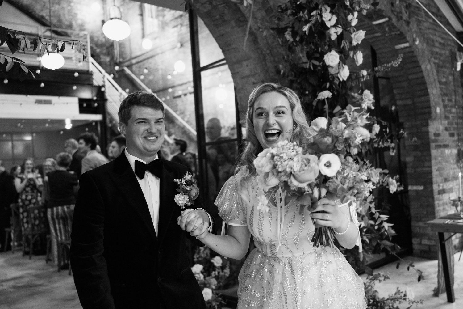 A vintage black and white wedding photo showing a celebration with flowers and brick arch decor.