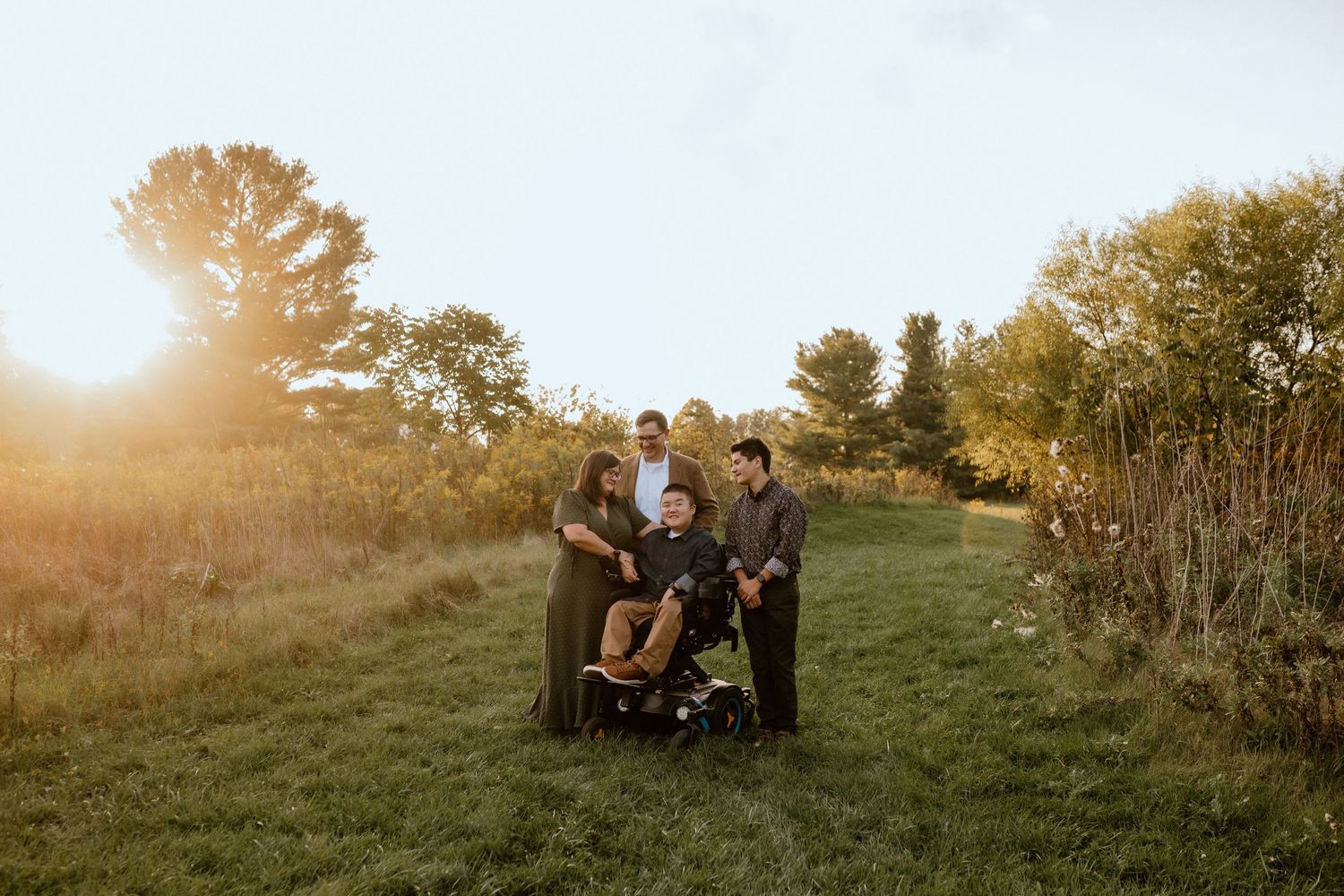 Family group photo in golden sunset light standing together on a grassy hill.