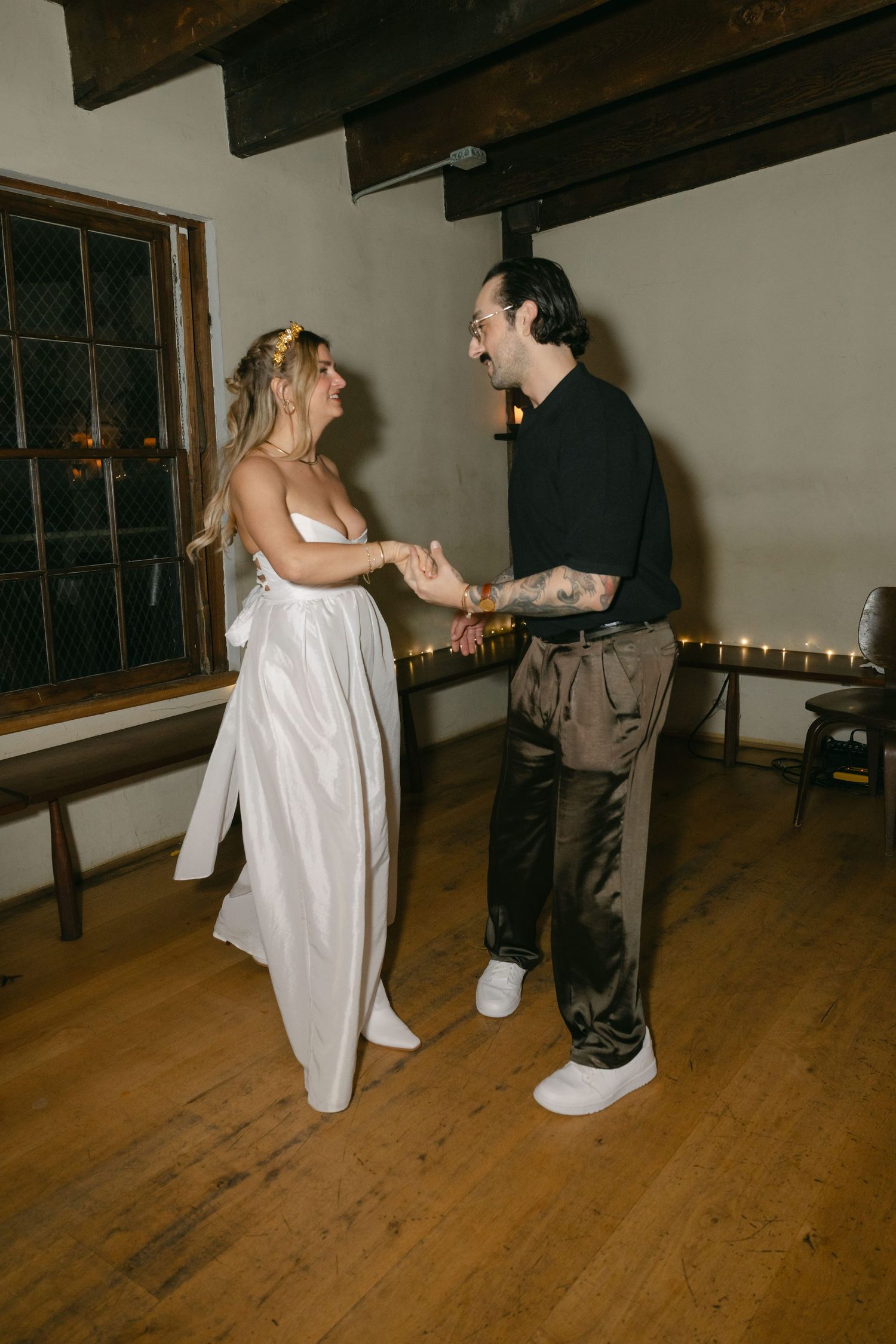 A couple shares a playful dance moment together at a wedding reception on a wooden floor.