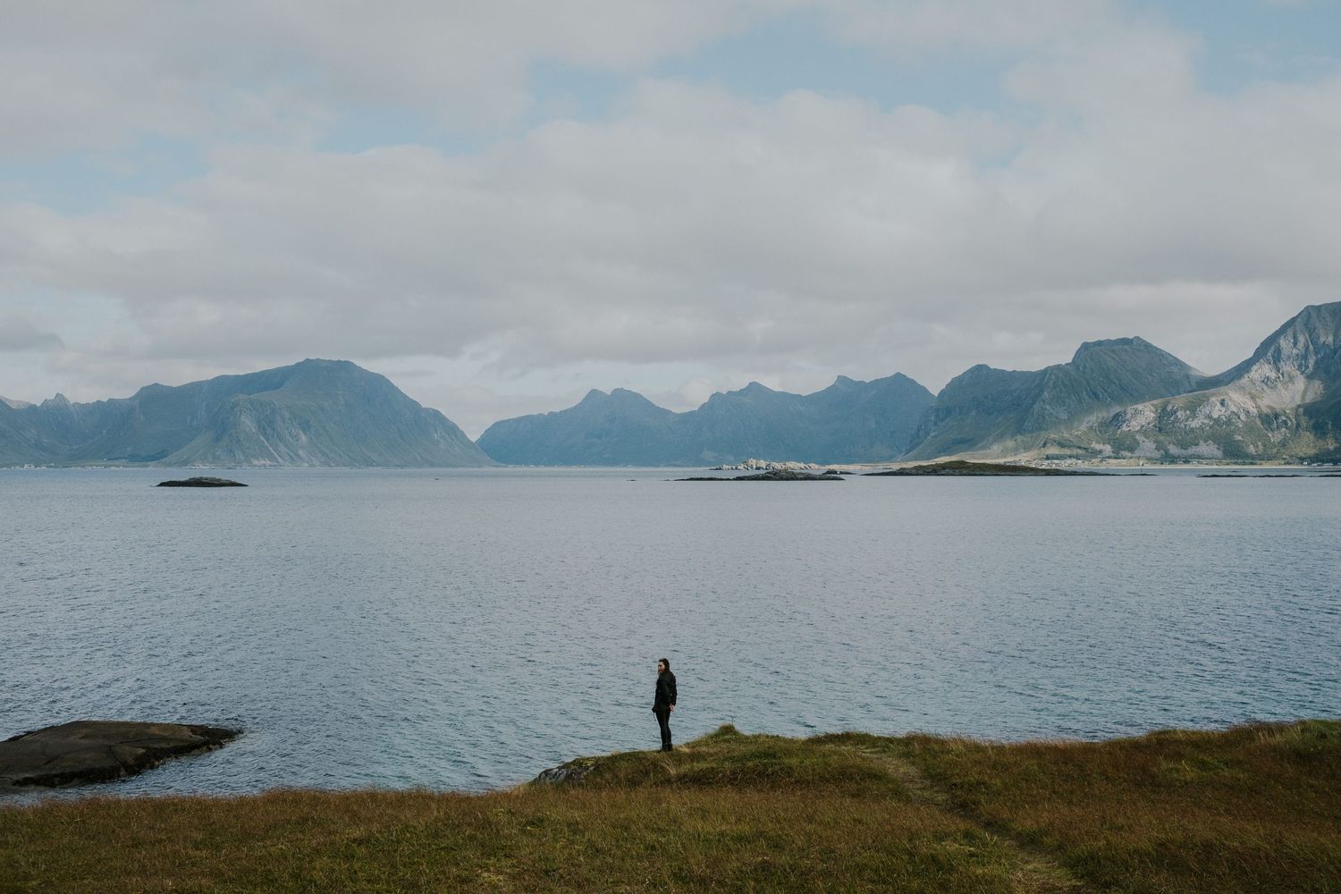 Silhouette of person standing on coastal cliff overlooking dramatic fjord landscape.