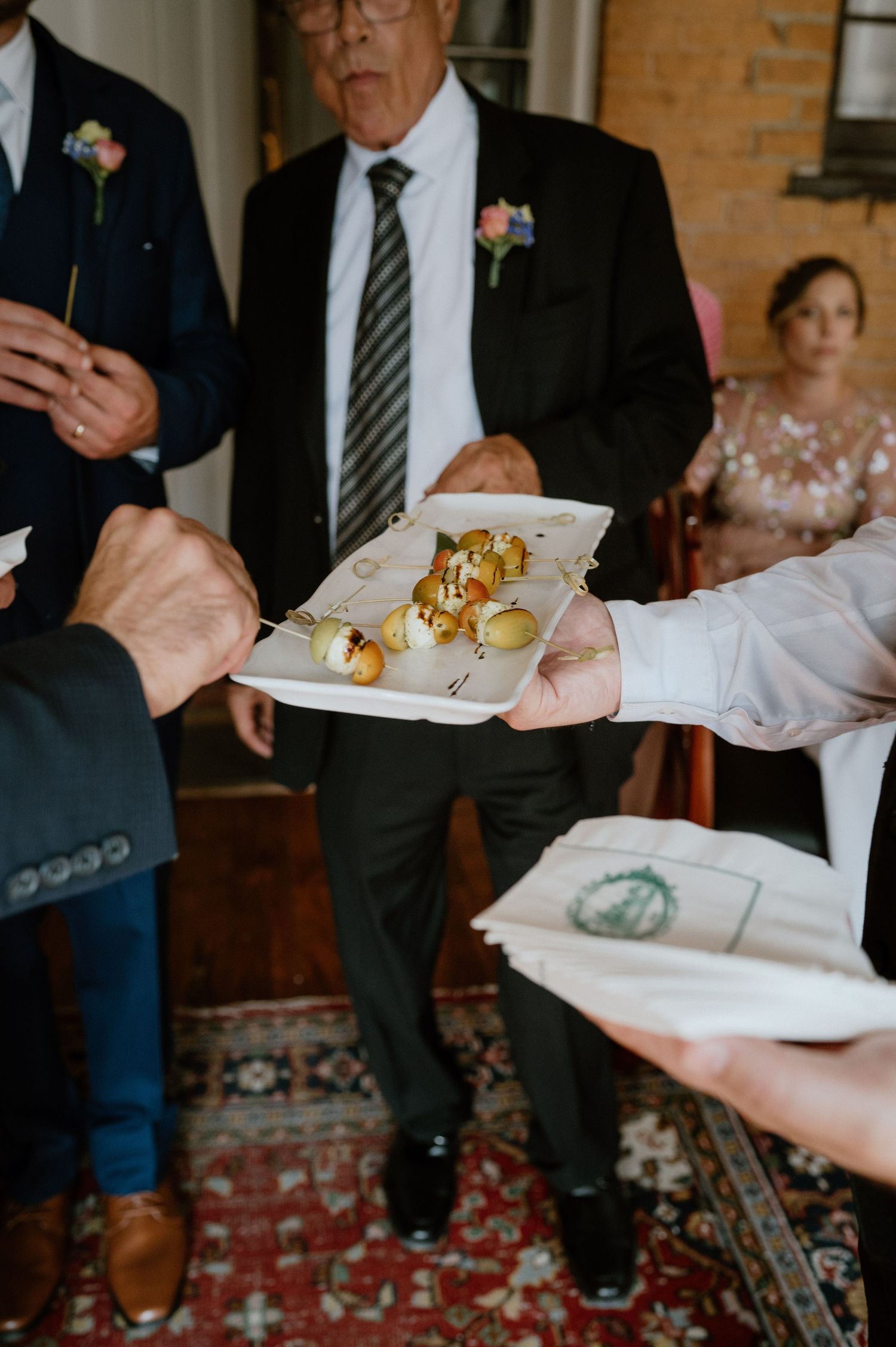 Wedding guests in formal attire passing appetizer plates at indoor reception.