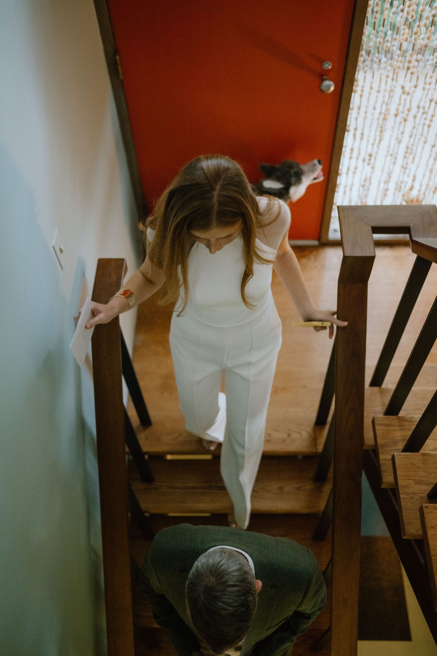Person in white descending wooden stairs with a red door in the background.