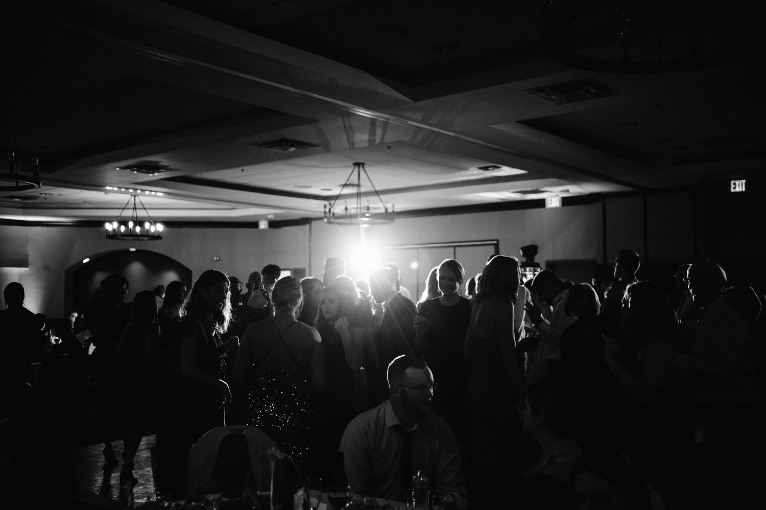 Dark silhouettes of wedding guests dancing under bright venue lighting.
